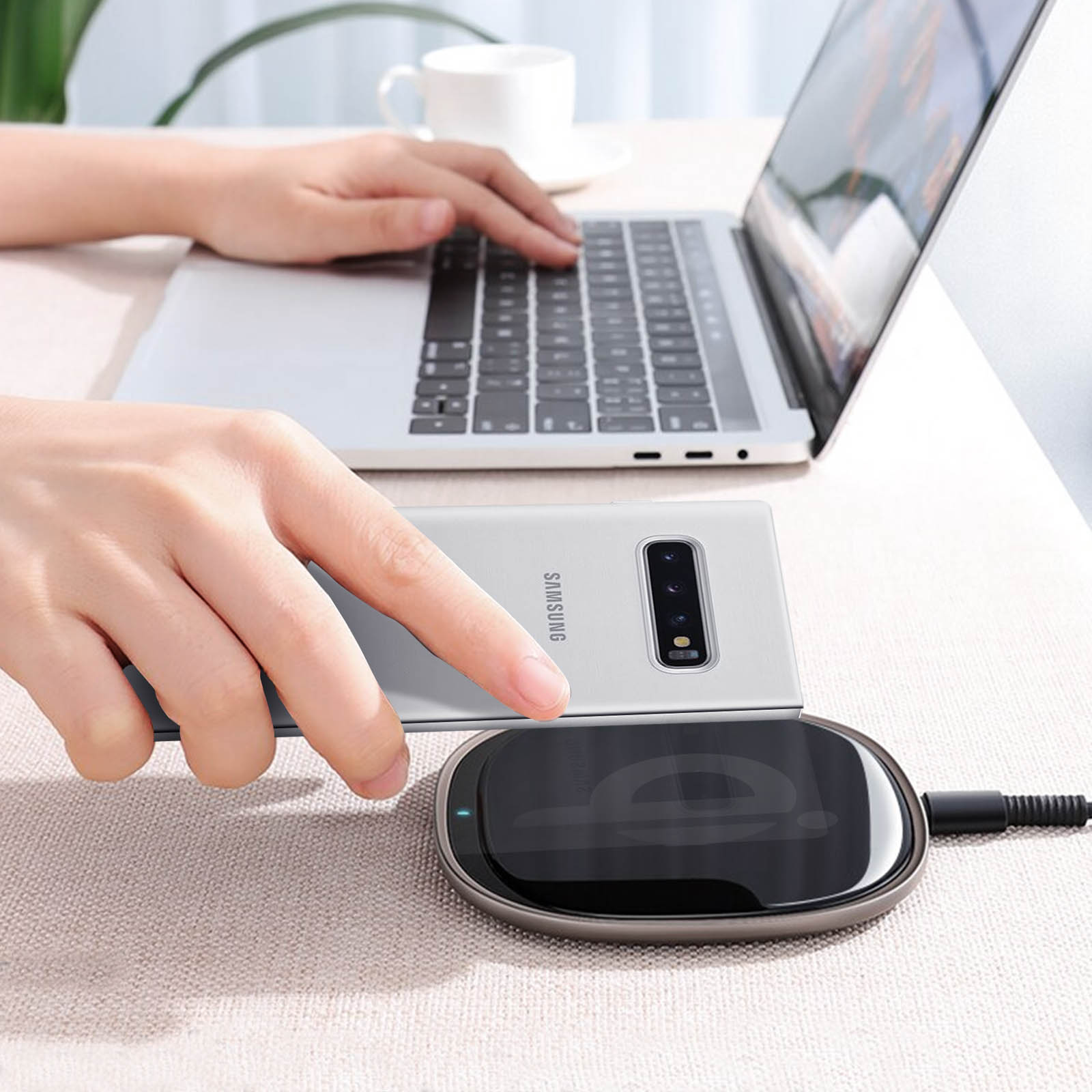 Una persona usando una laptop con un teléfono en un cargador inalámbrico. El teléfono es un Samsung plateado.