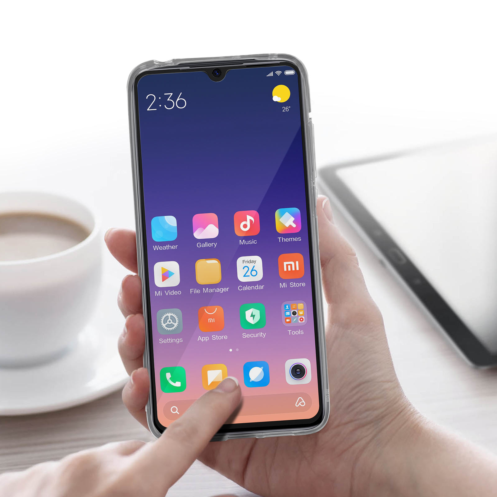 Hand hält Telefon mit Icons auf dem Bildschirm. Tasse und Tablet daneben.