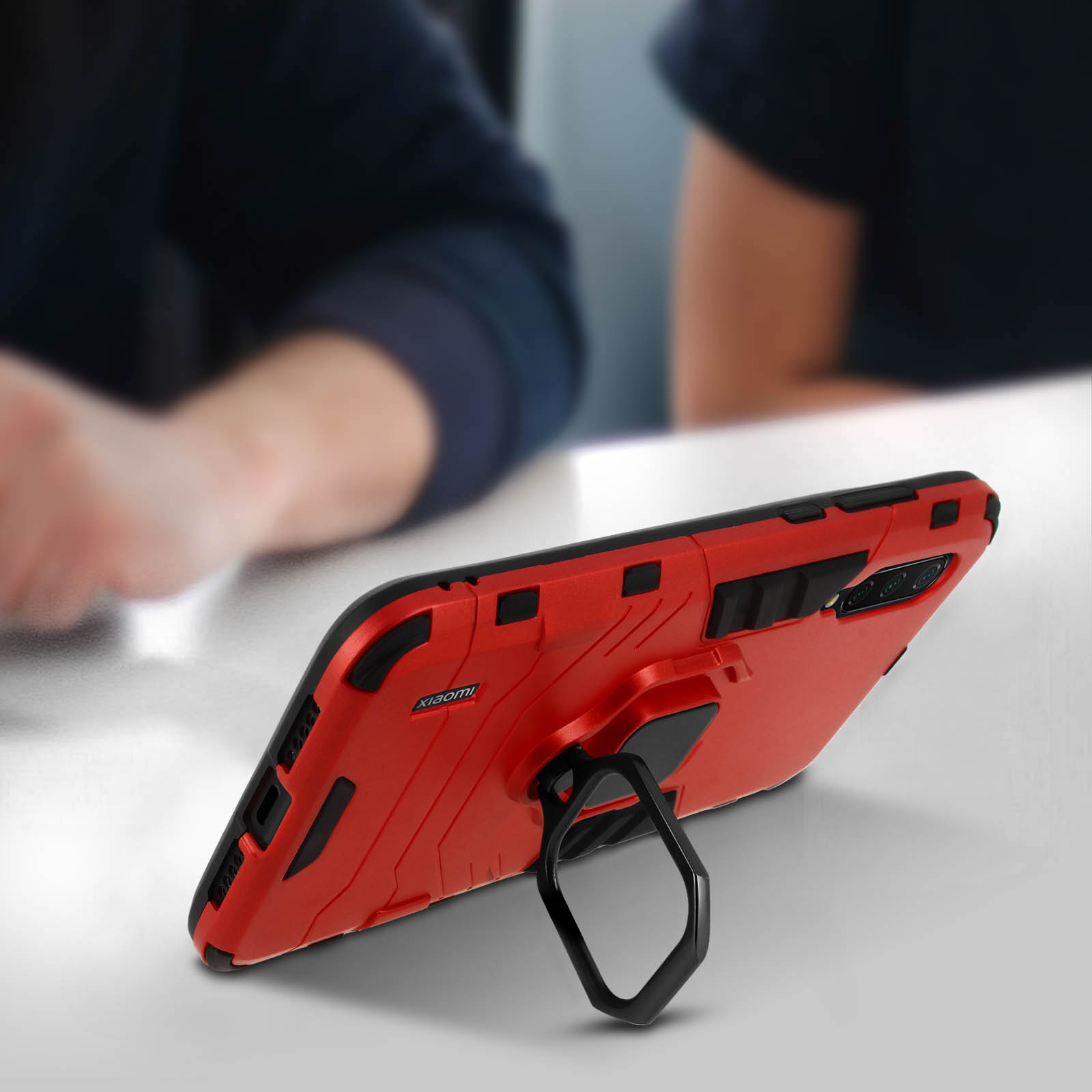 Custodia per telefono rossa con anello di supporto, angolata su un tavolo bianco. Lo sfondo è un interno sfocato.