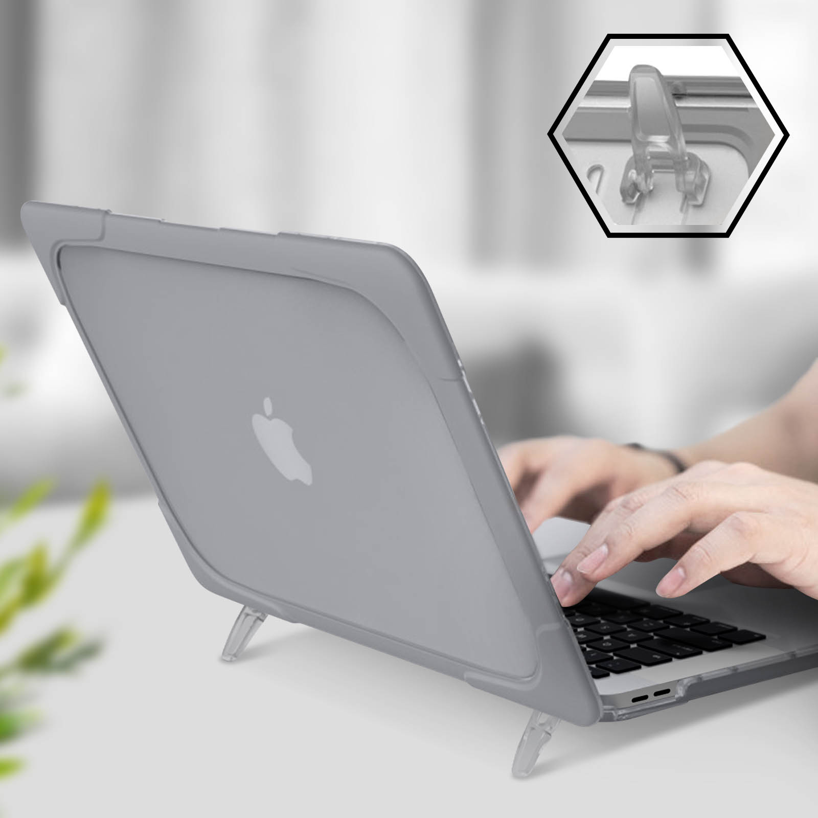 Laptop in grauer Hülle auf weißer Oberfläche, Hände auf der Tastatur, Nahaufnahme des Scharniers.