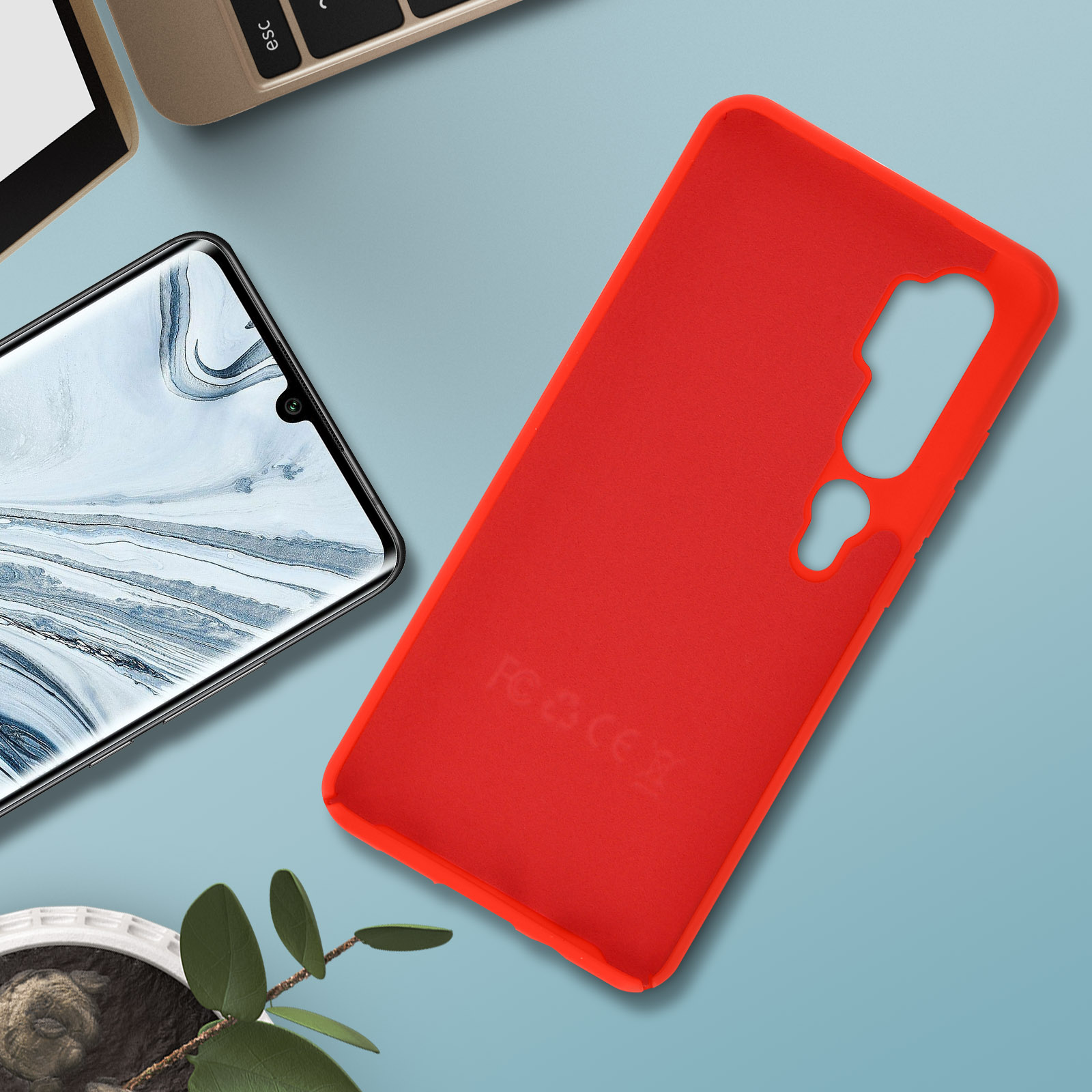 Custodia rossa per telefono, telefono e foglie su una superficie blu.