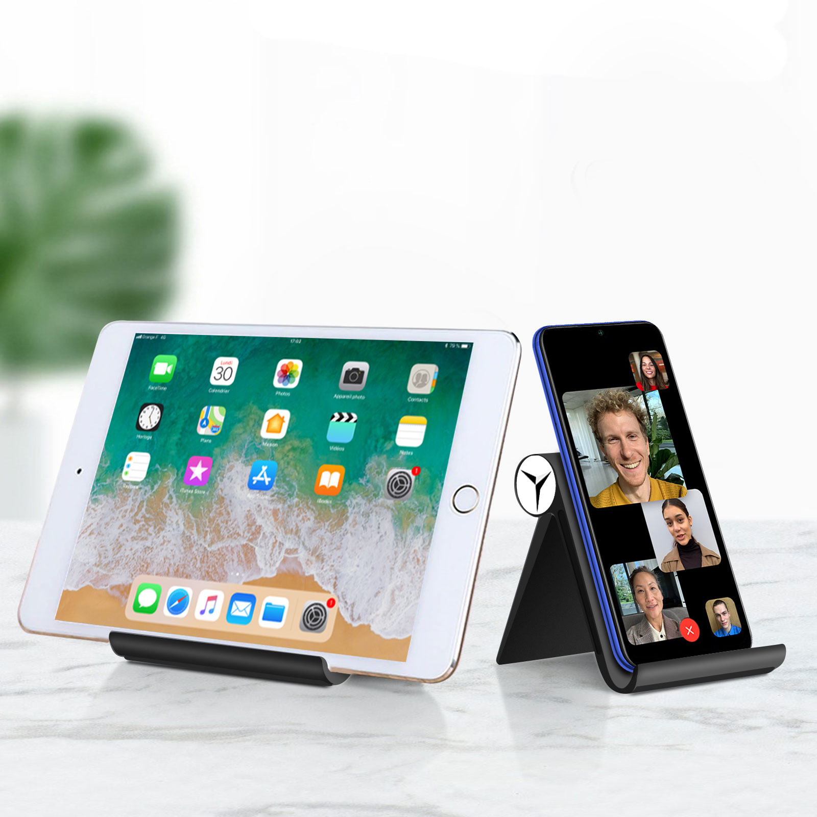 Due dispositivi su supporti: un tablet e un telefono che mostra una videochiamata. Su una superficie bianca.