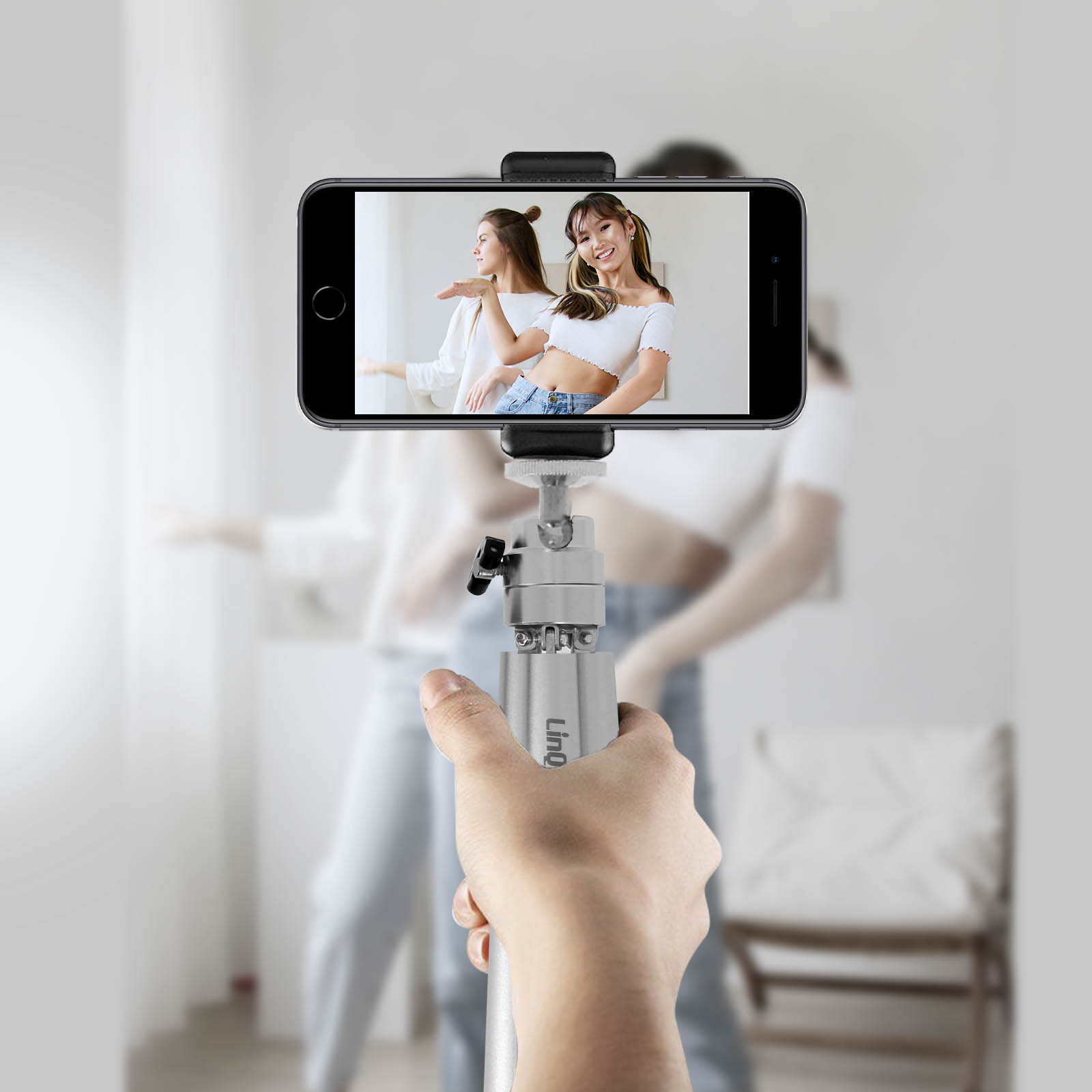 Una mano sosteniendo un trípode con un teléfono que muestra a dos mujeres.