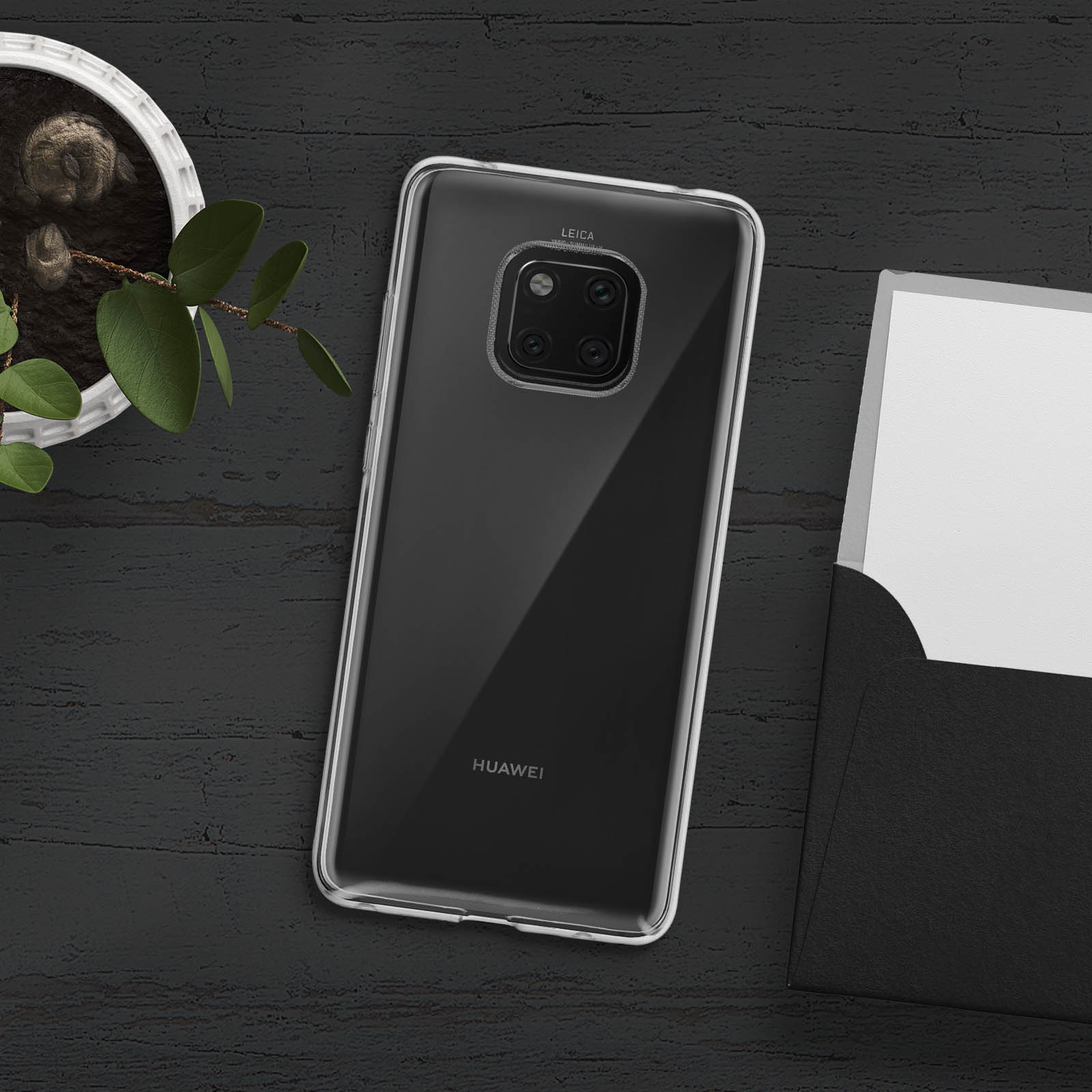 Schwarzes Telefon mit durchsichtiger Hülle, auf dunkler Holzoberfläche, mit Pflanze und Karte.