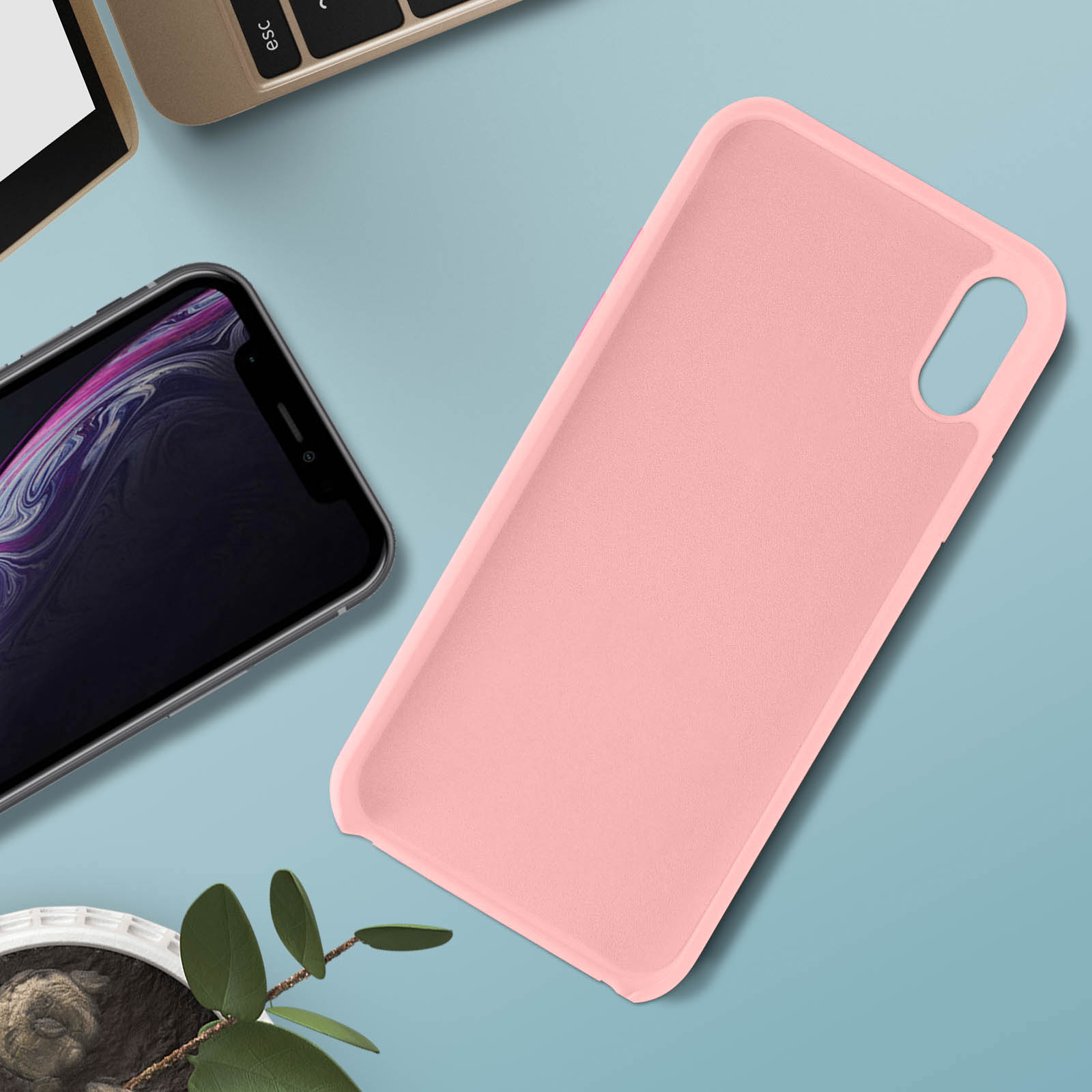 Roze telefoonhoes op een oppervlak. Telefoon erin, met een laptop en plant op de achtergrond.