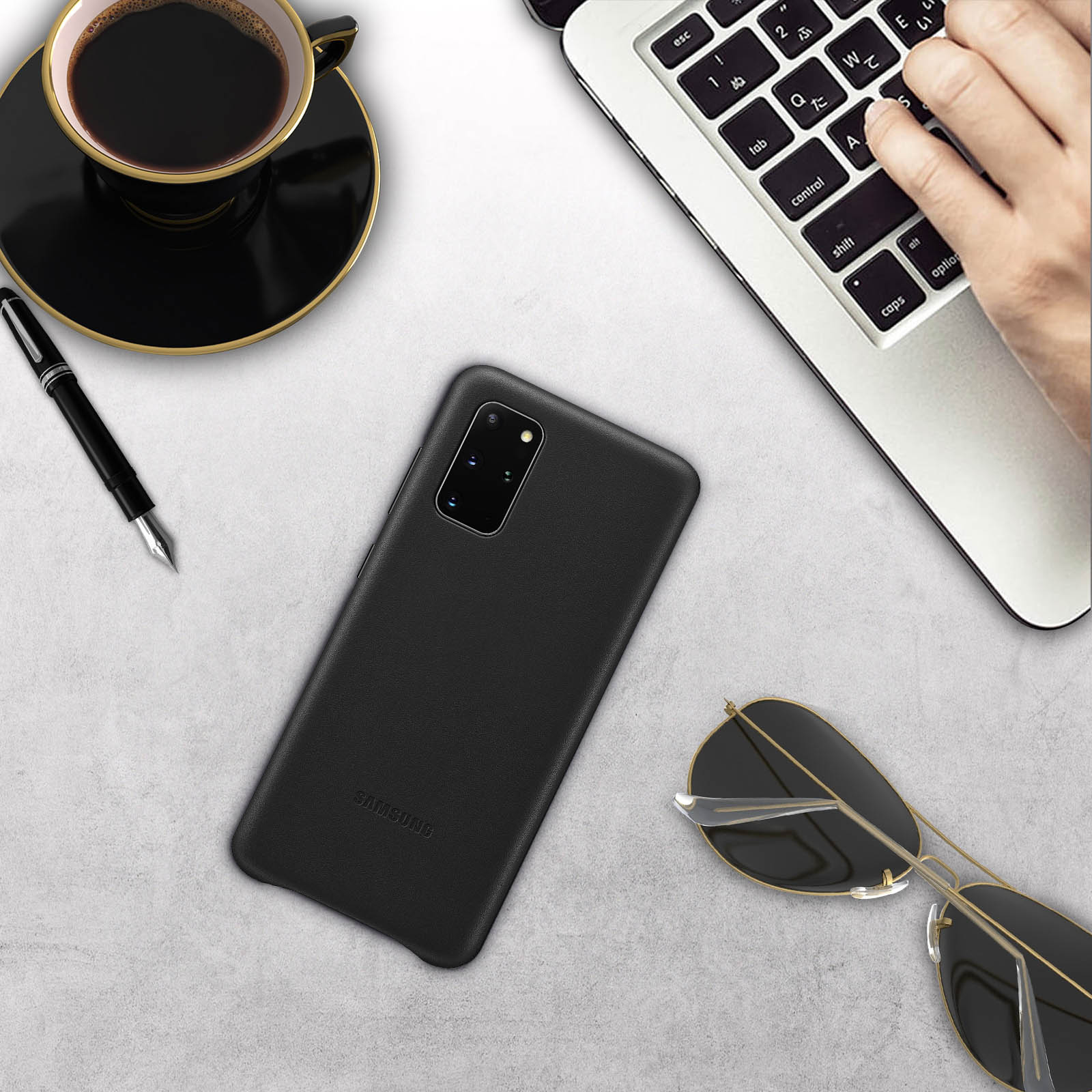 Teléfono en una mesa con accesorios. Café, bolígrafo, gafas y portátil visibles.