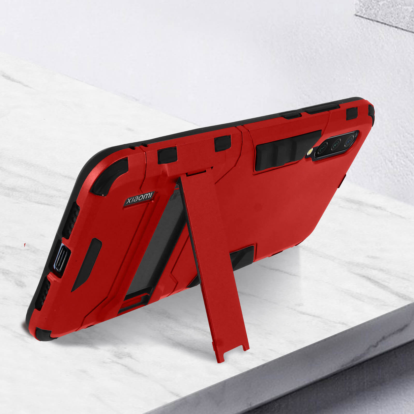 Custodia per telefono rossa con supporto, posizionata su una superficie di marmo. Custodia con dettagli neri e logo Xiaomi.