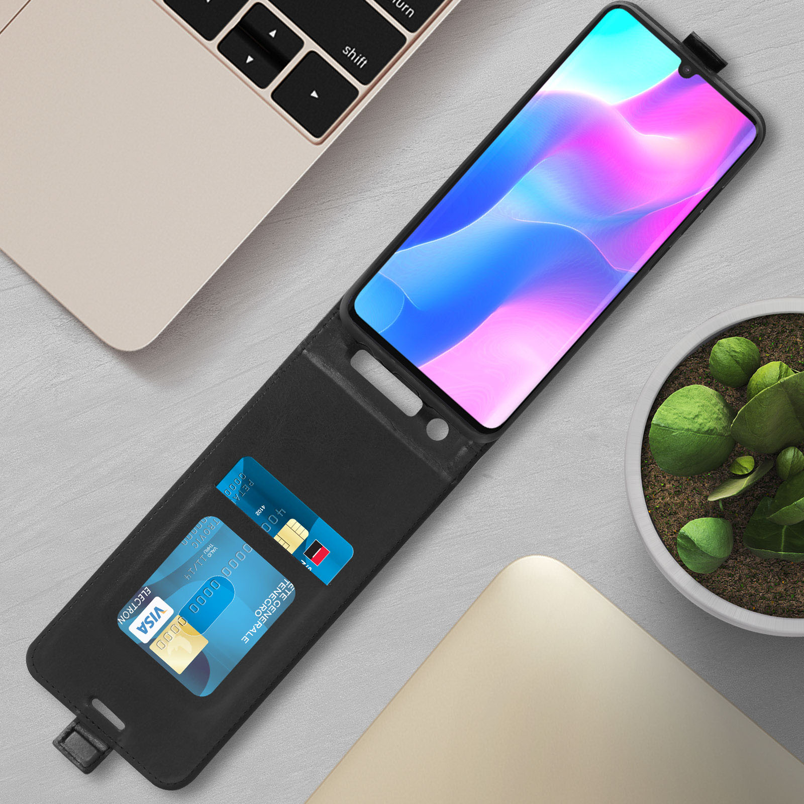 Custodia nera per telefono, aperta, con carte di credito visibili. Un laptop e una pianta sullo sfondo.