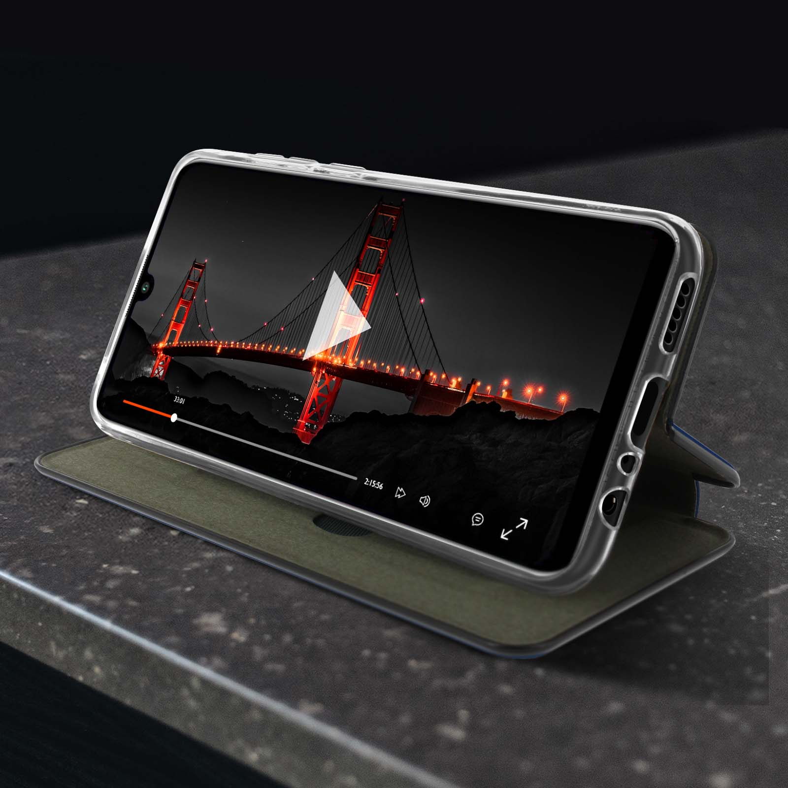 Telefono in custodia, mostra un video di un ponte di notte. Custodia aperta su un tavolo.