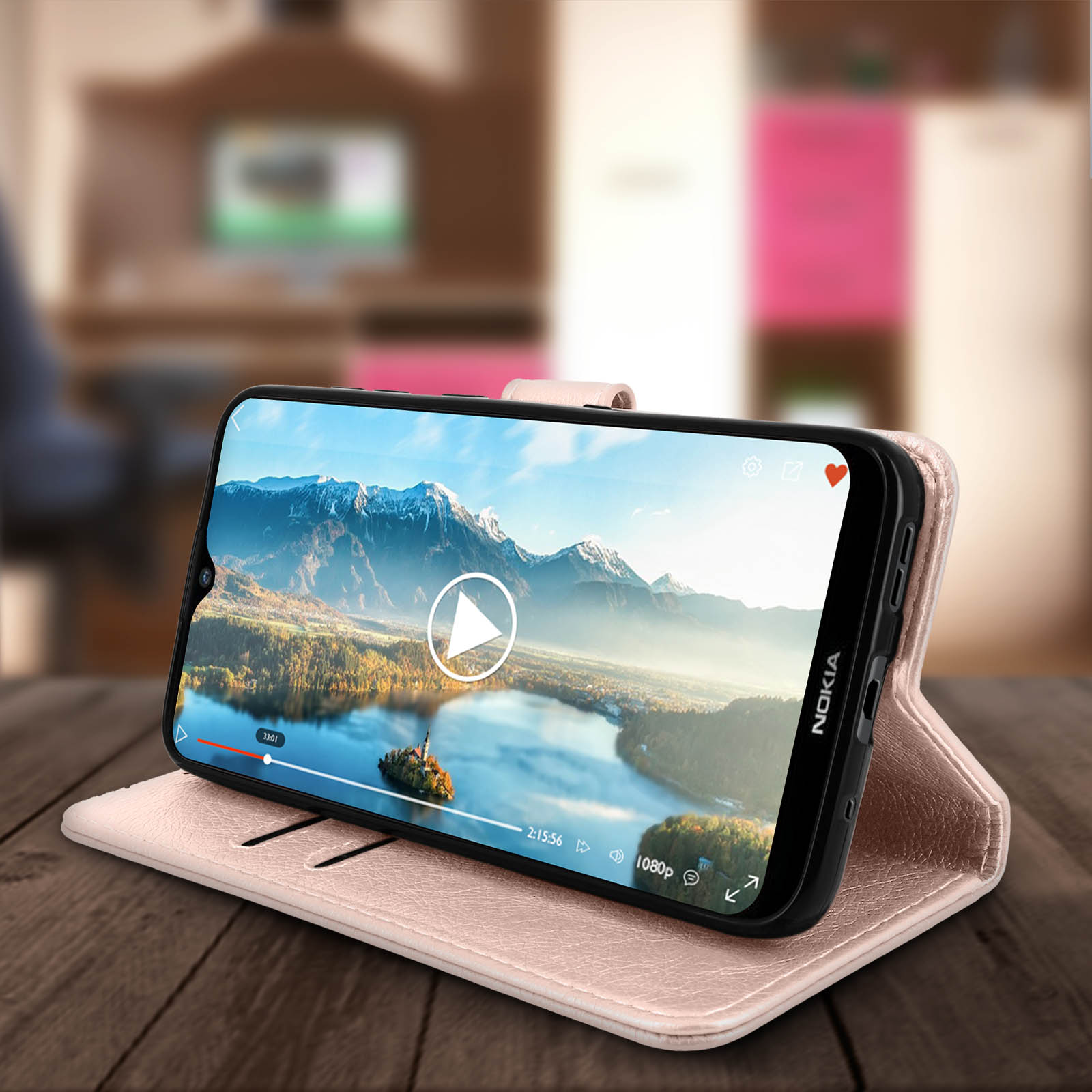 Un telefono con un video in riproduzione è in una custodia rosa su un tavolo di legno.