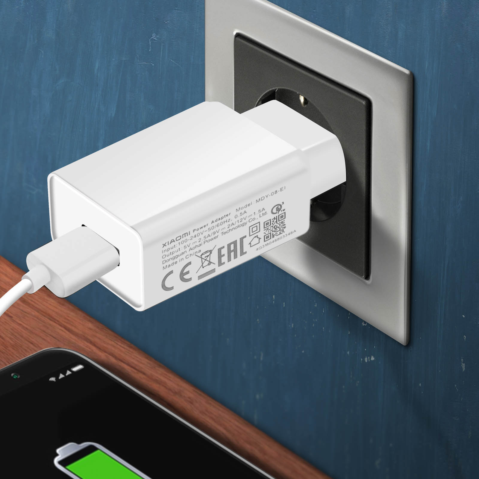 Un caricabatterie bianco è collegato a una presa a muro. Un telefono è sotto il caricabatterie, in carica.