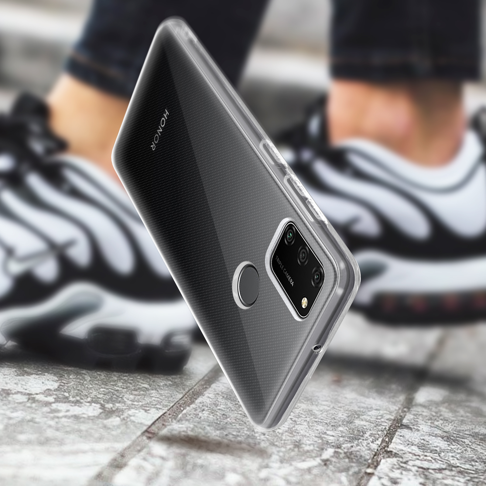 Smartphone dans un étui transparent, tenu contre un arrière-plan flou de jambes et de pieds d'une personne.