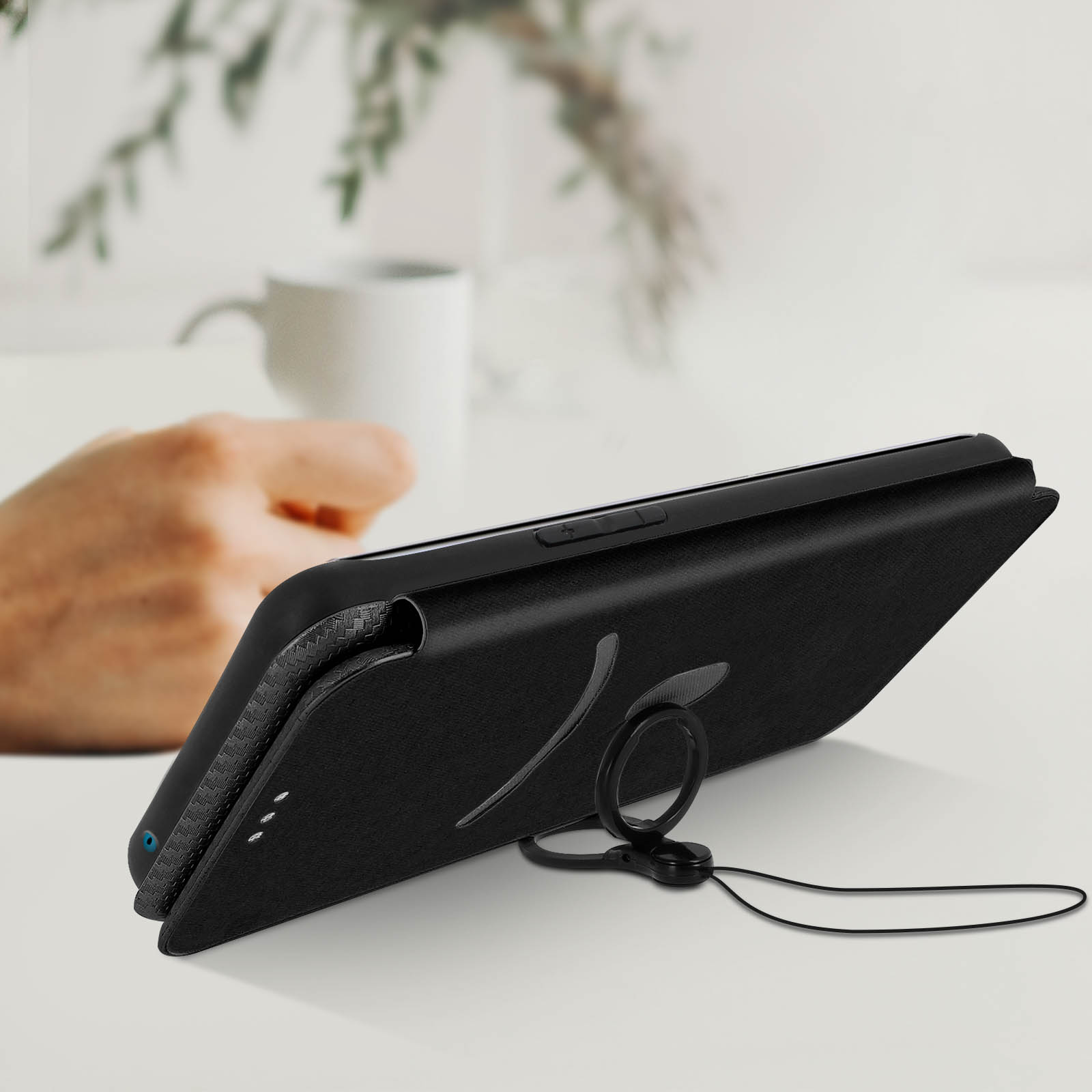 Custodia nera per telefono con un anello di supporto. Il telefono è su un tavolo con una tazza bianca sullo sfondo.