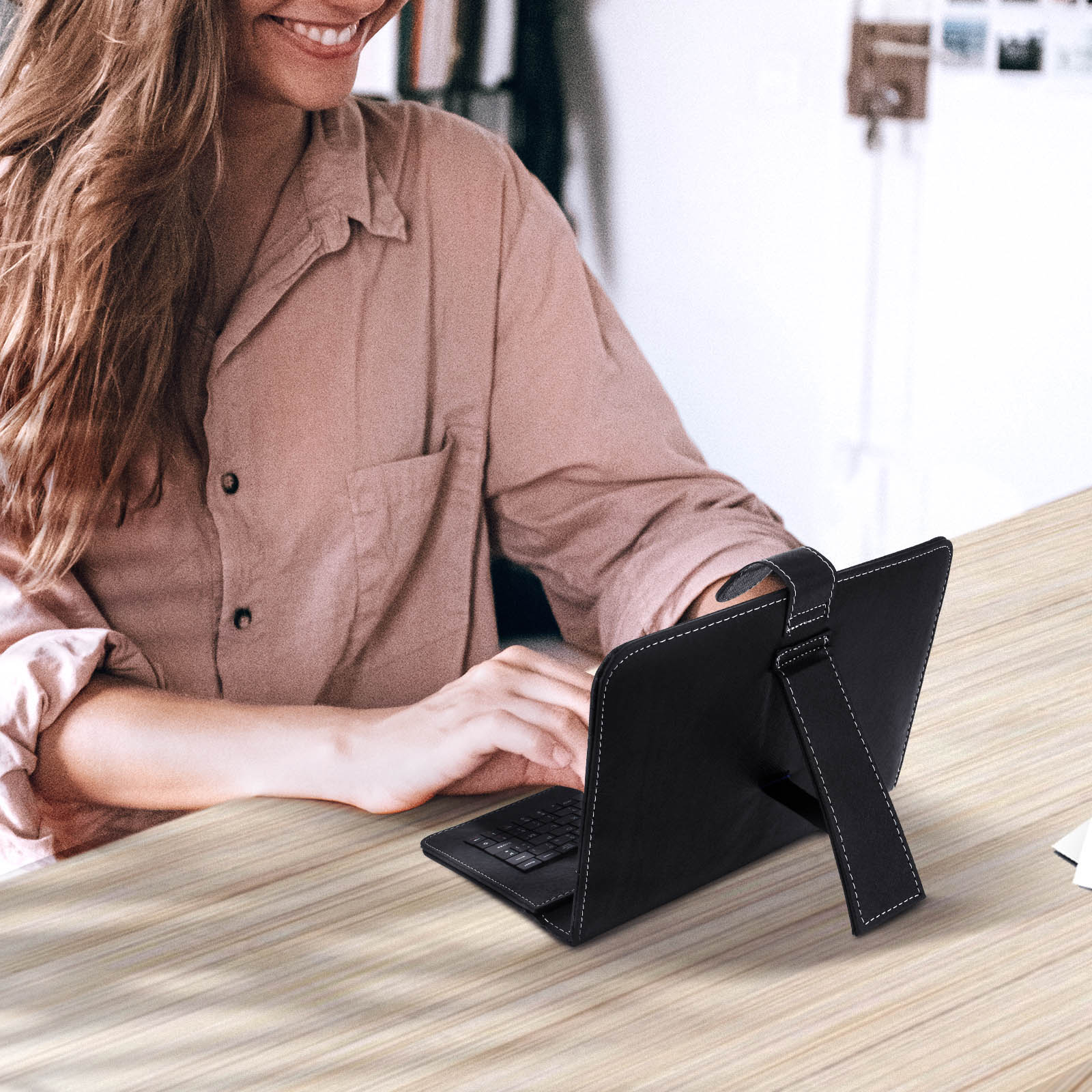 Una mujer está usando un teclado de tableta negro sobre una mesa de madera. Ella está sonriendo.