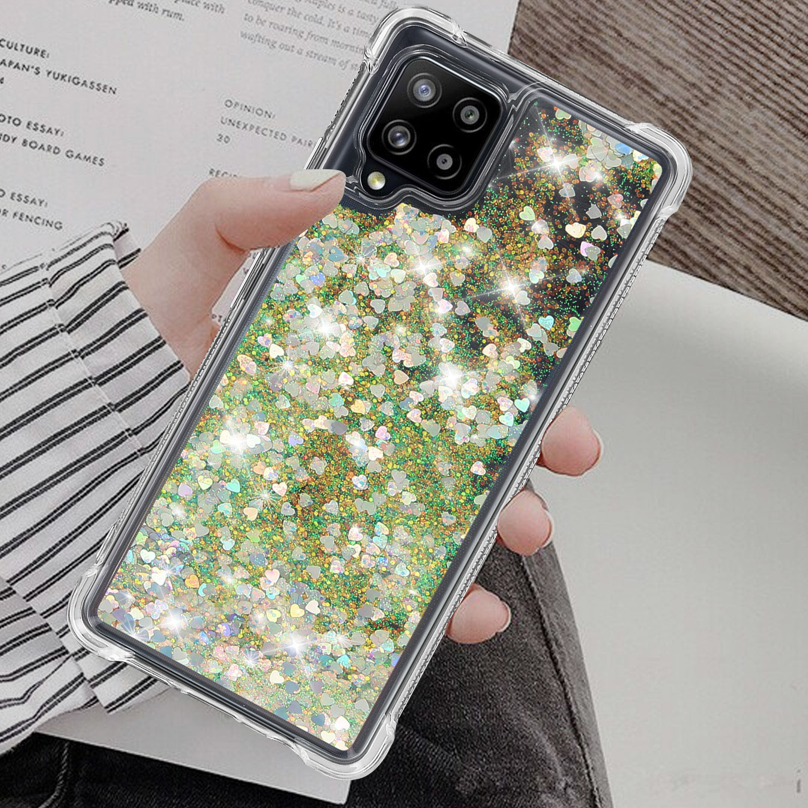 Una mano che tiene un telefono con una custodia trasparente piena di glitter e alcune pagine stampate sullo sfondo.