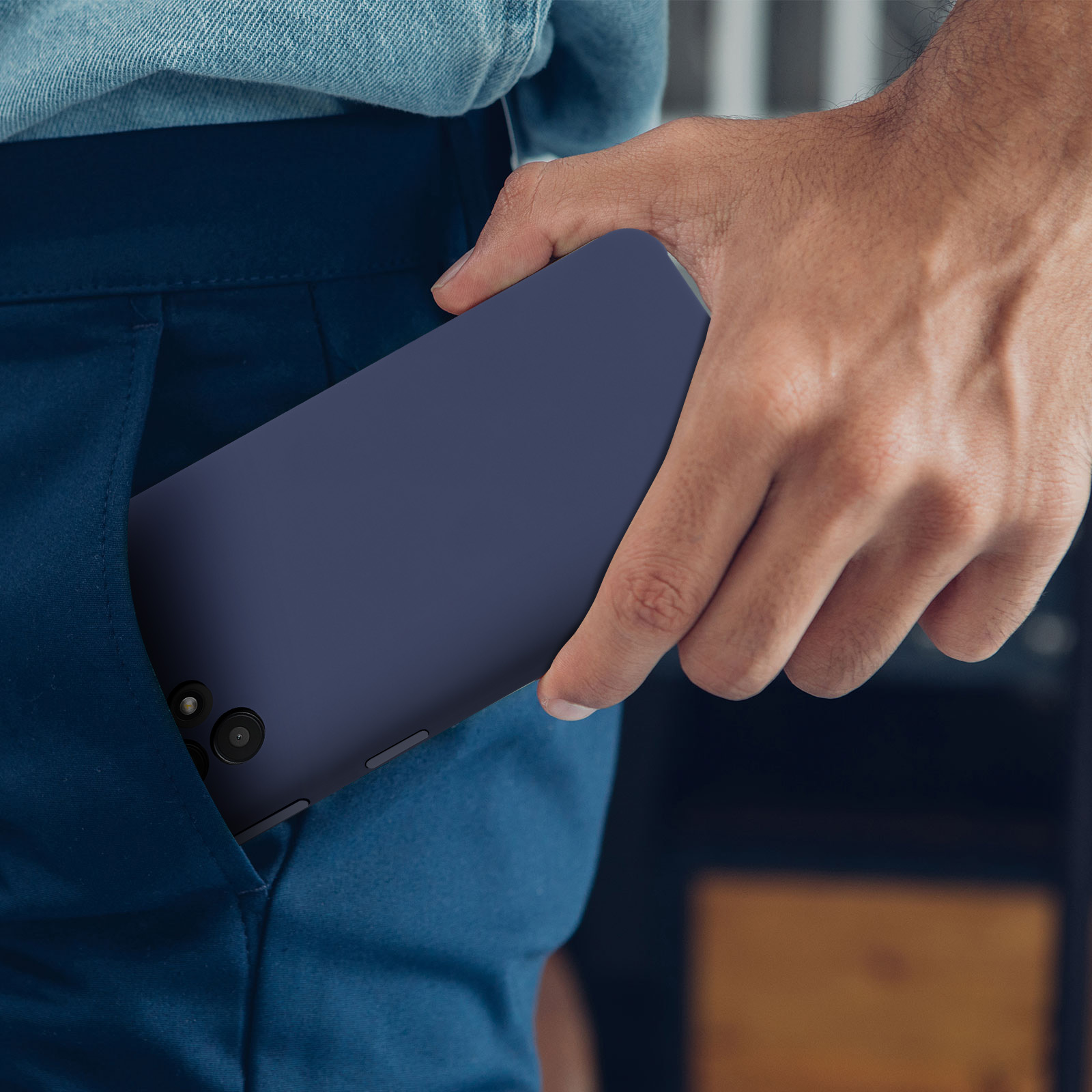 Eine Hand steckt ein marineblaues Telefon in eine Tasche einer blauen Hose.