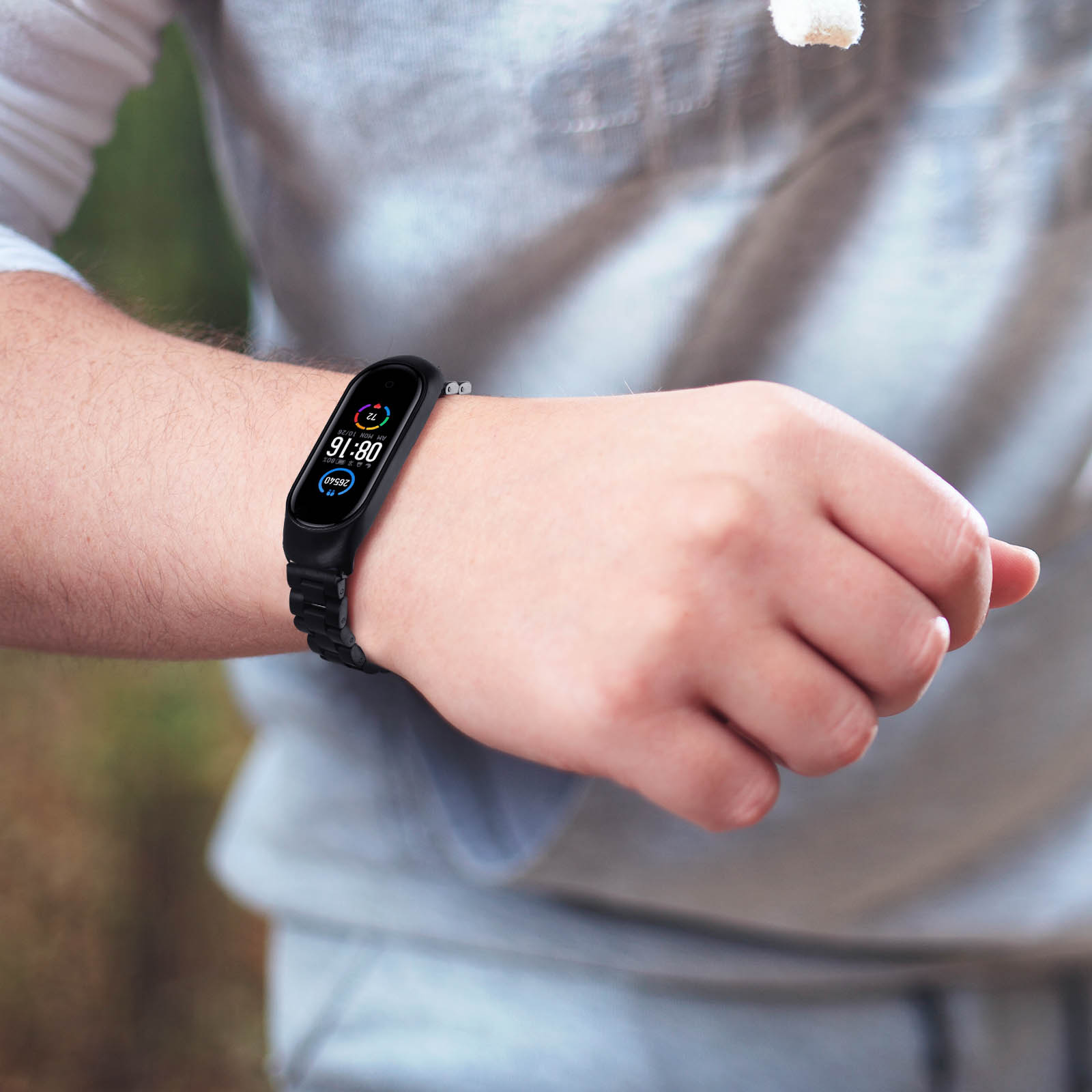 Polso di uomo con uno smartwatch nero. Il display mostra l'ora e la frequenza cardiaca. Sfondo grigio.