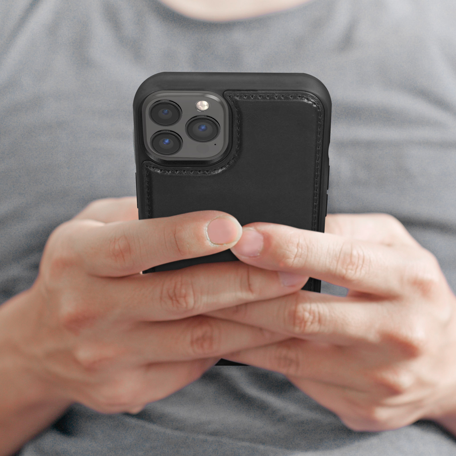 Eine Person hält ein Telefon. Das Telefon hat eine schwarze Lederhülle. Drei Kameralinsen sind sichtbar.