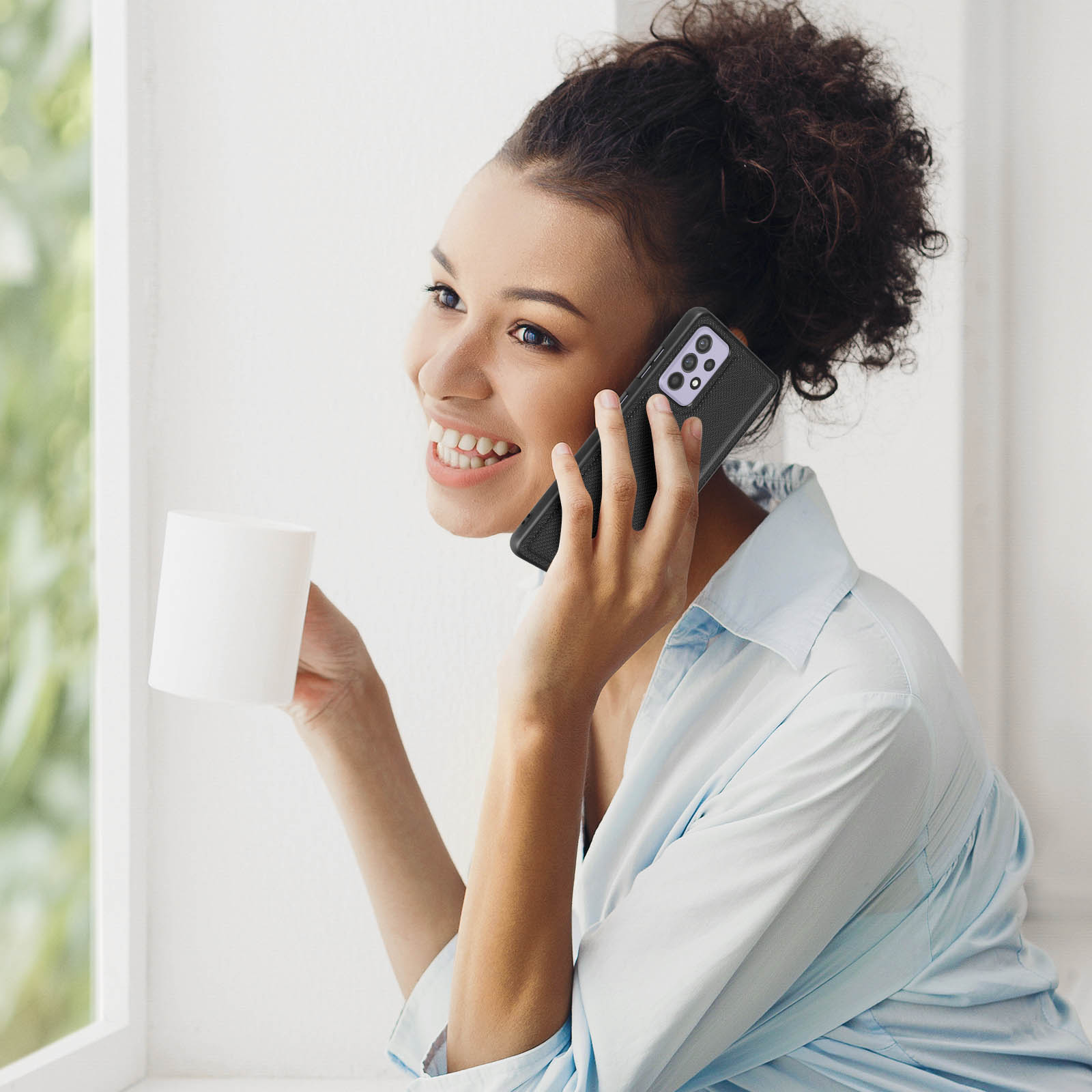 Eine Frau benutzt ein Telefon, lächelt, in der Nähe eines Fensters.
