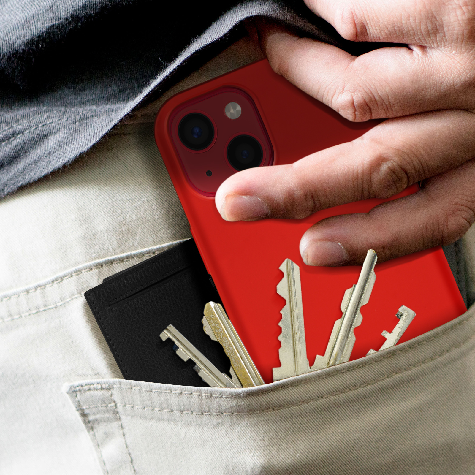 Mano che mette un telefono in tasca con chiavi e un portafoglio nero. Pantaloni beige.