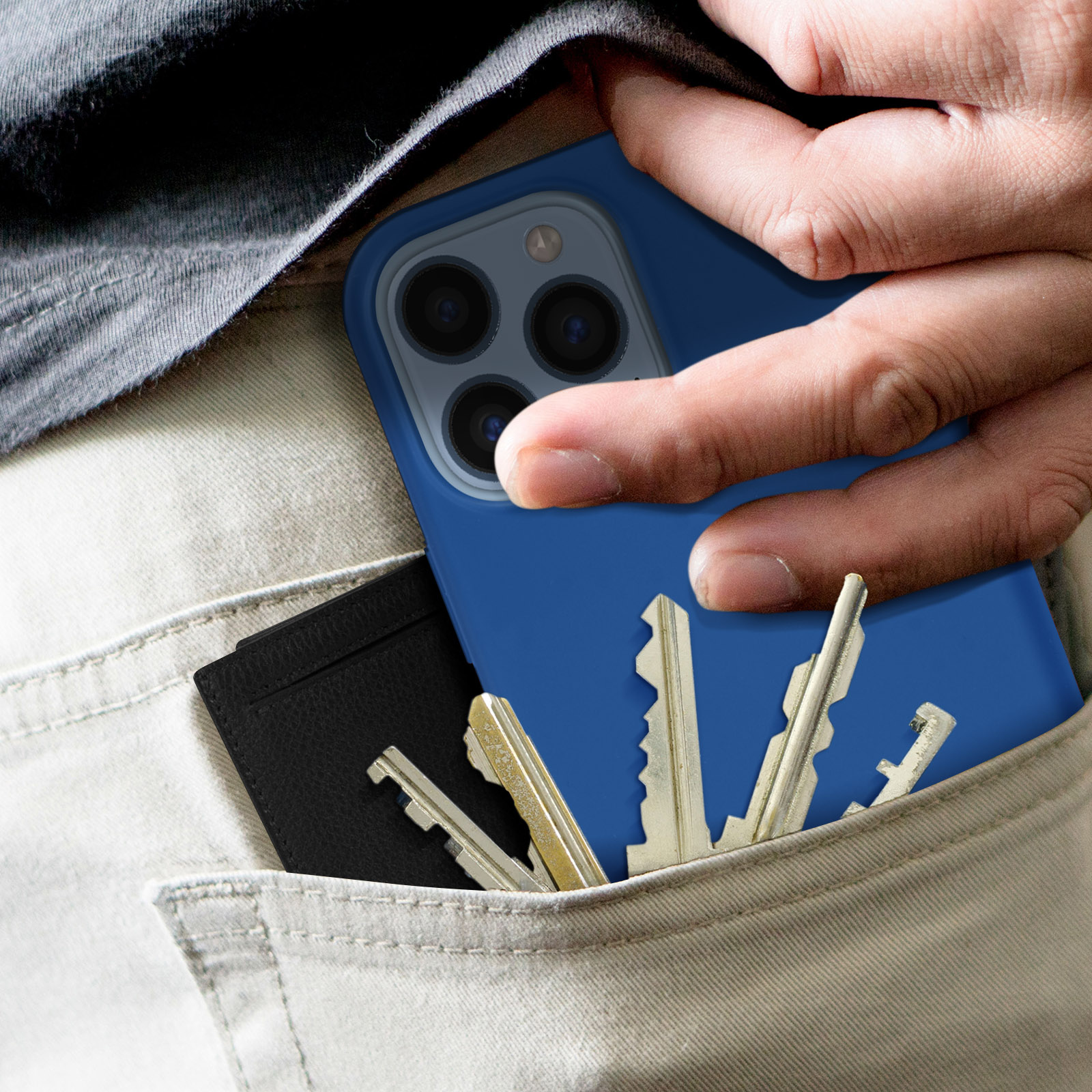 La main d'une personne dans une poche avec un téléphone bleu et des clés. Un portefeuille noir est également visible.