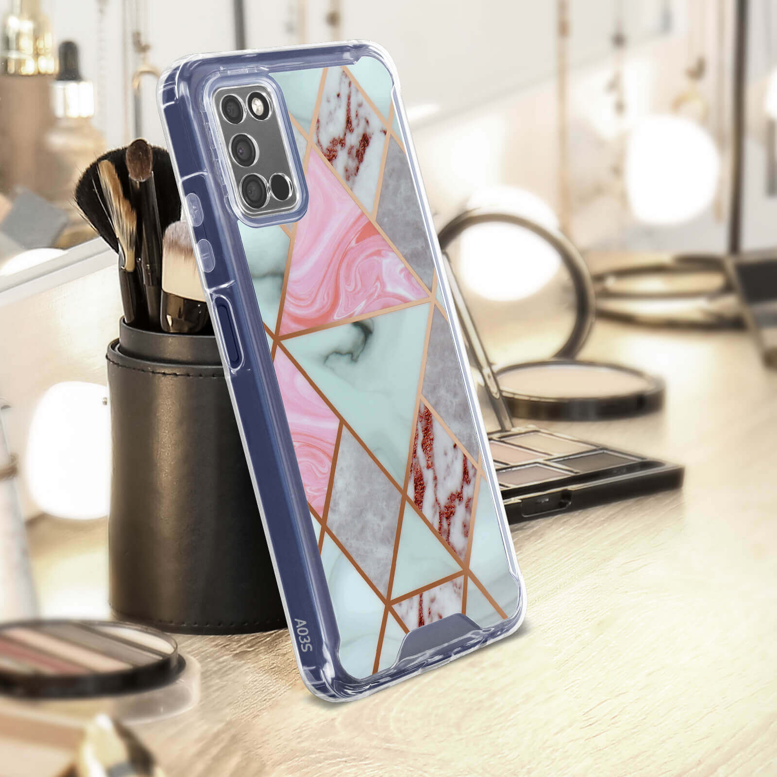 Een telefoon in een hoesje met een marmerontwerp, op een tafel met make-up kwasten en andere items.