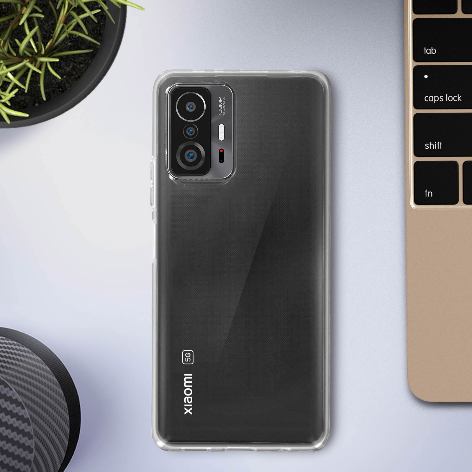 Una custodia trasparente per telefono su un telefono nero su una superficie chiara, con un laptop visibile.