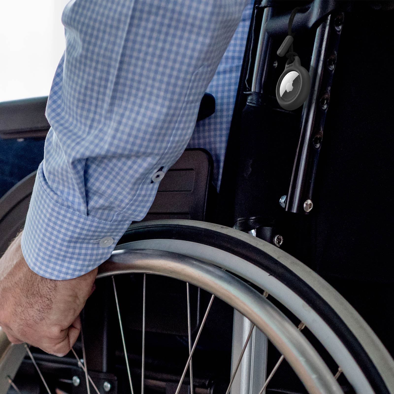 Osoba na wózku inwalidzkim trzymająca koło. AirTag jest przymocowany do krzesła. Tło jest rozmyte.
