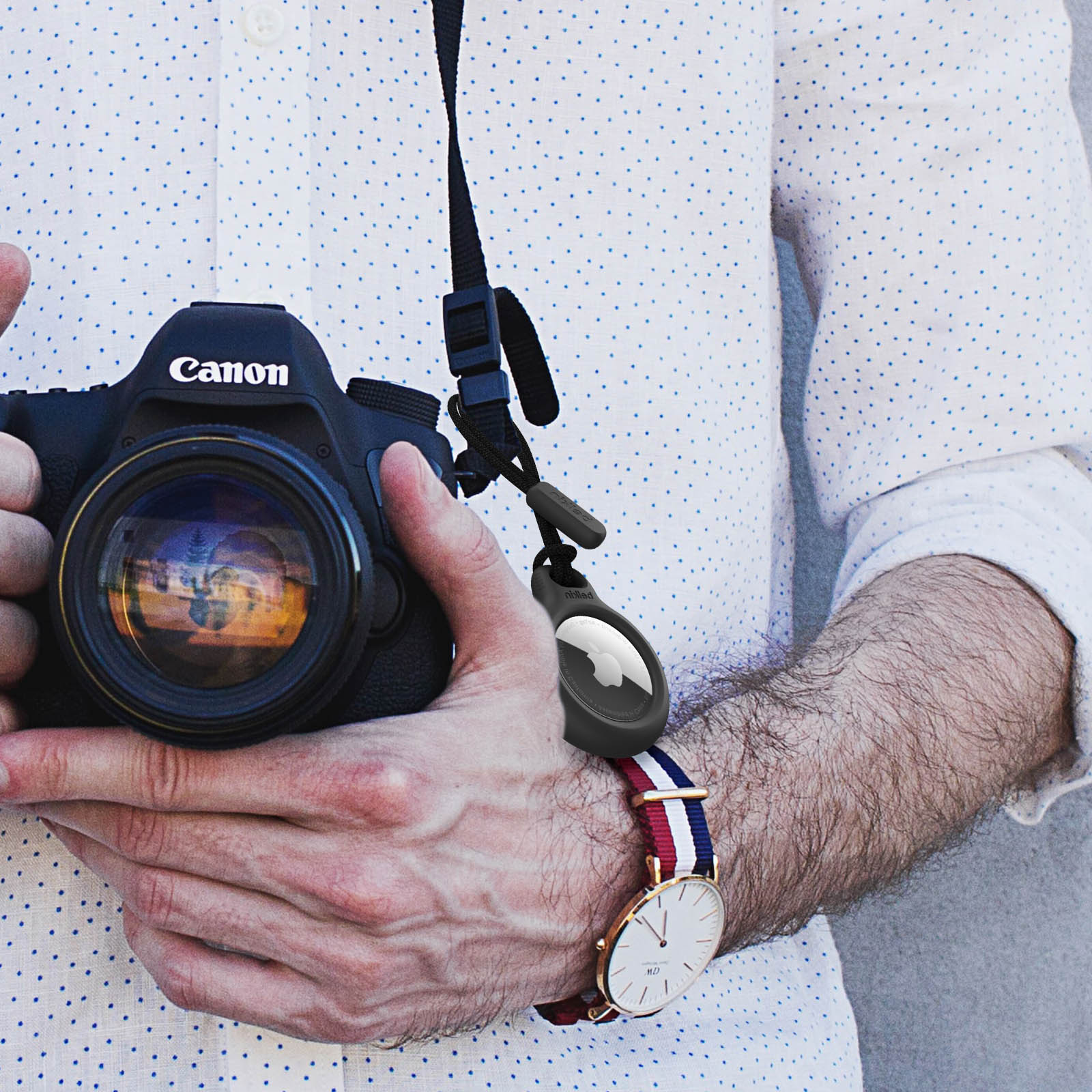 Mężczyzna trzymający aparat Canon z podłączonym AirTagiem, noszący zegarek.
