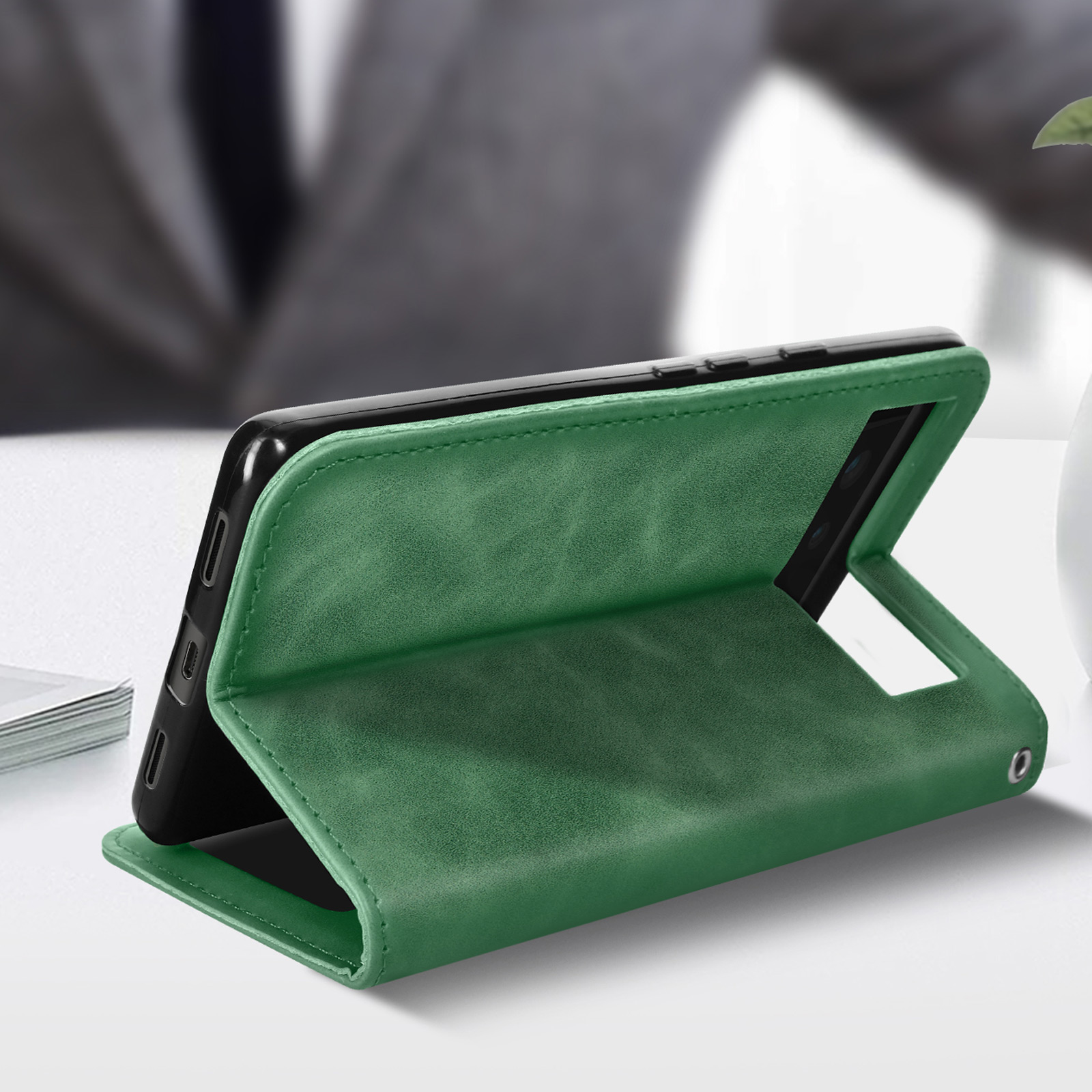 Groene leren telefoonhoes, open, met de telefoon erin. Het ligt op een wit oppervlak.