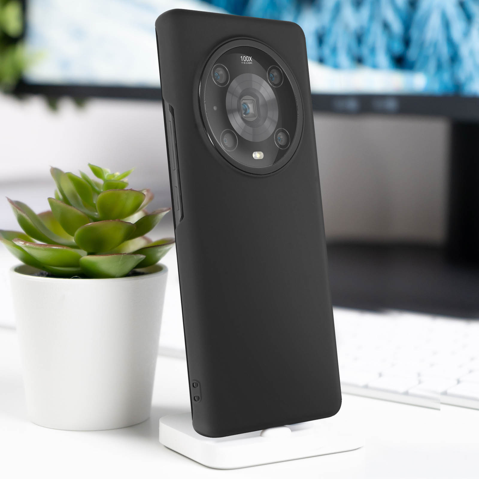 Un telefono nero su un supporto bianco, vista posteriore. Il telefono ha un grande modulo fotocamera circolare ed è su una scrivania.