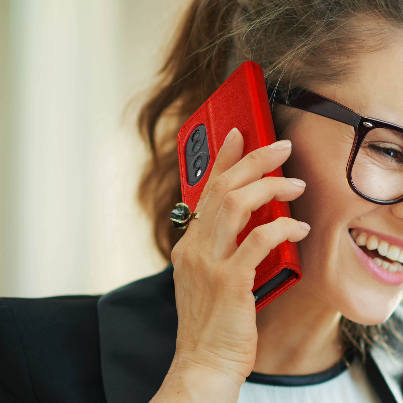 Donna con gli occhiali sorride mentre tiene una custodia rossa del telefono all'orecchio, al telefono.