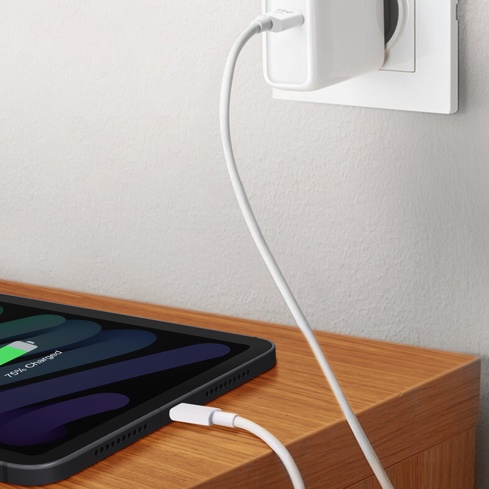 Ein Tablet wird aufgeladen. Ein weißes Ladekabel ist an das Tablet und eine Steckdose angeschlossen.