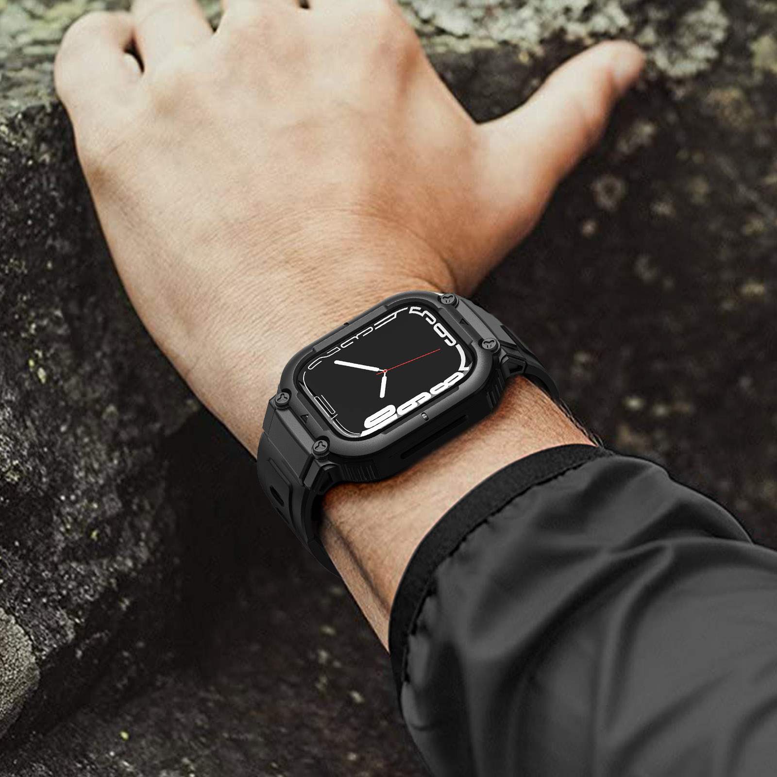 La mano de una persona lleva un reloj negro con una correa negra, sobre un fondo rocoso.