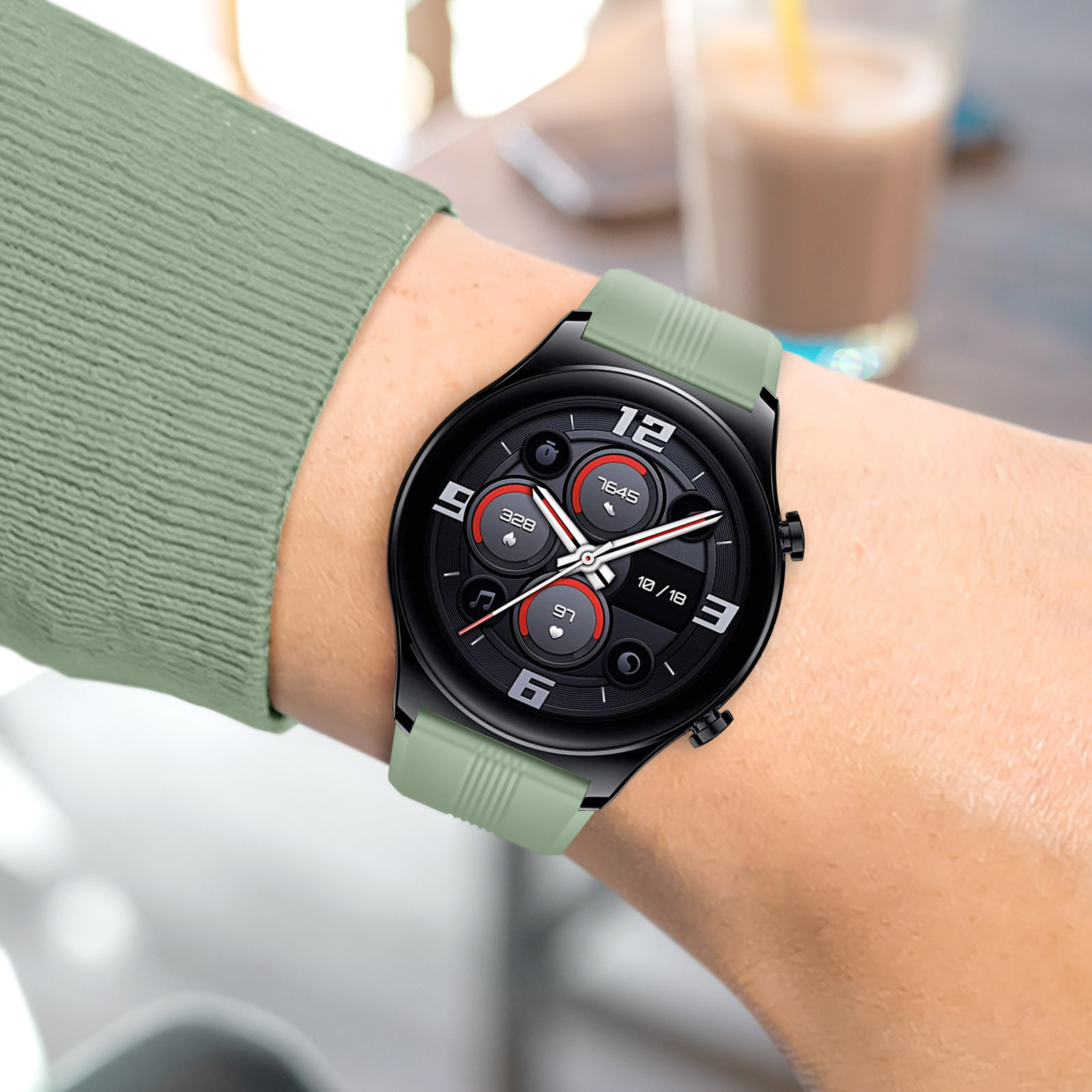 Una mano que lleva un smartwatch negro con una correa verde. La pantalla muestra la hora y los datos.