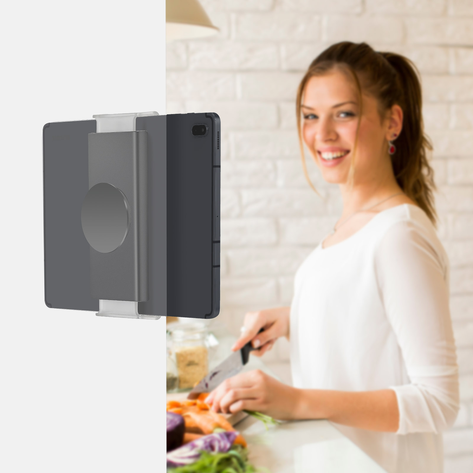 Tablet jest przymocowany do ściany za pomocą etui. Kobieta uśmiecha się, krojąc warzywa w tle.