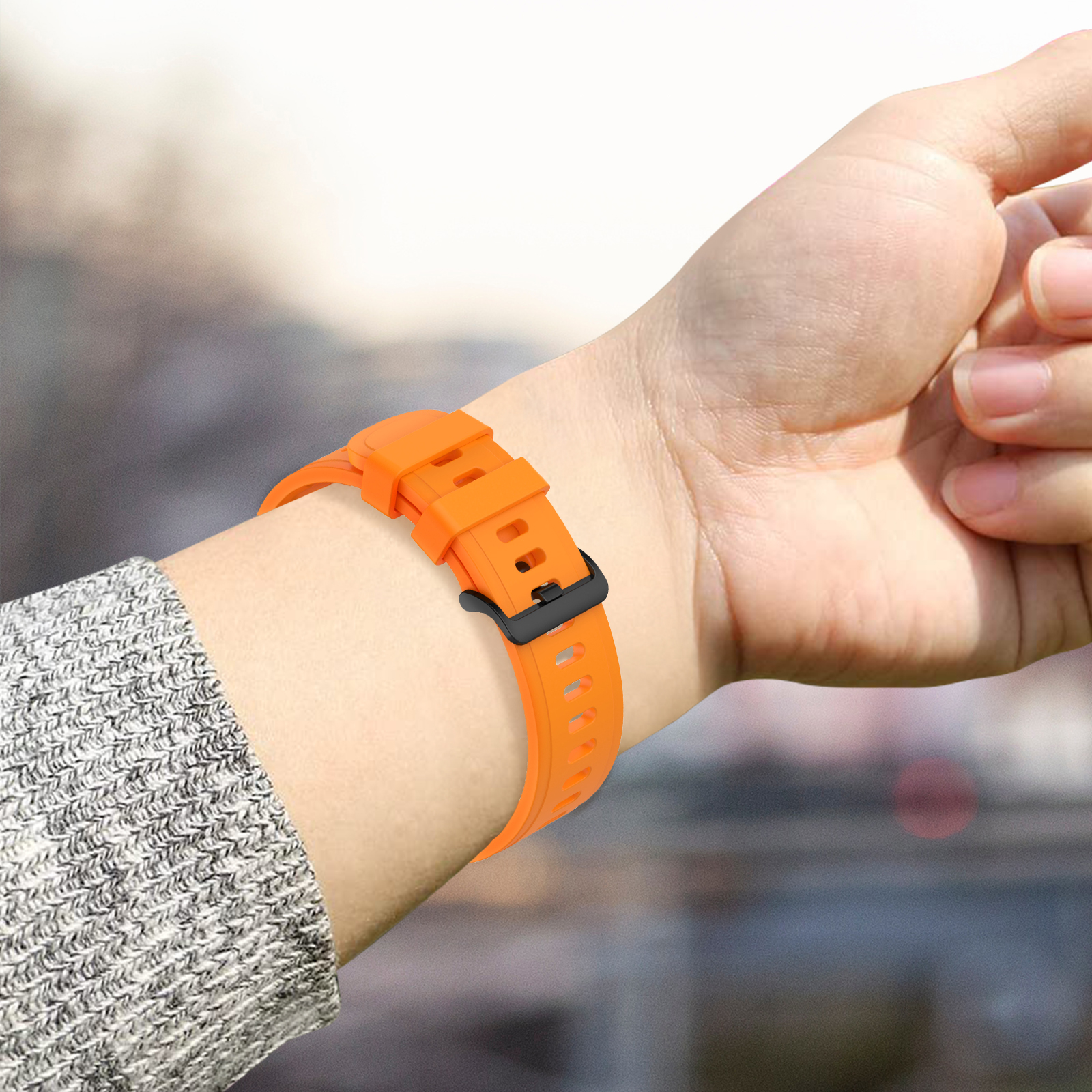 Muñeca con correa de reloj naranja. La correa está unida a un reloj con hebilla negra.