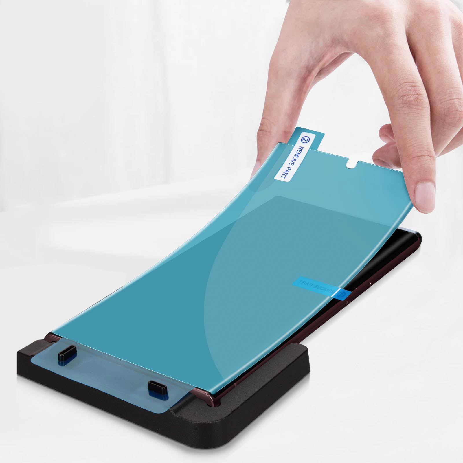 Una mano stacca la pellicola protettiva dallo schermo di un telefono. Lo schermo è su un supporto nero.