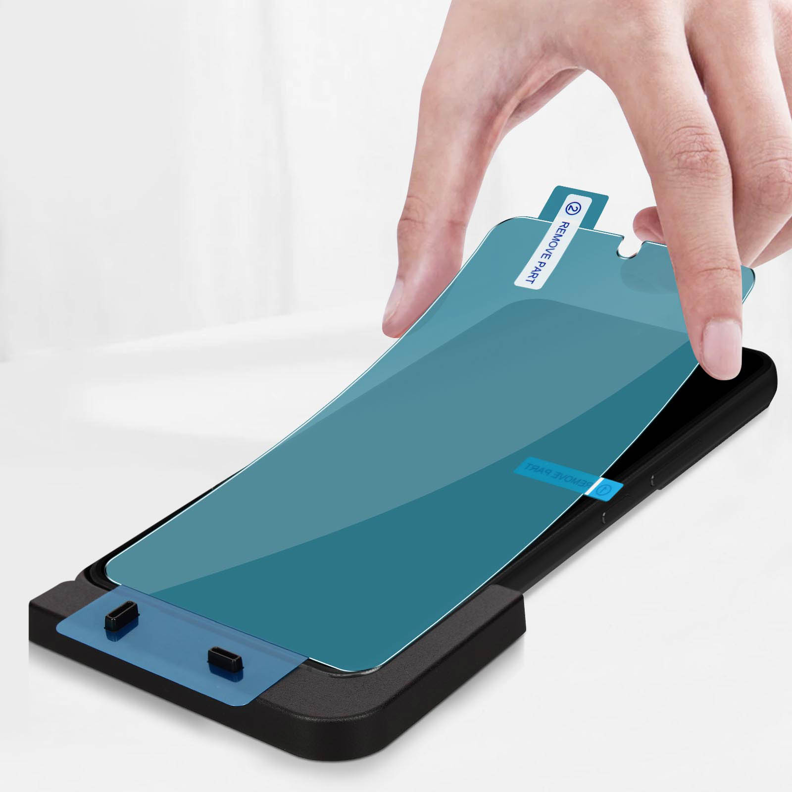 Mano che applica la protezione schermo a un telefono nero. Pellicola blu sul protettore. Sfondo bianco.