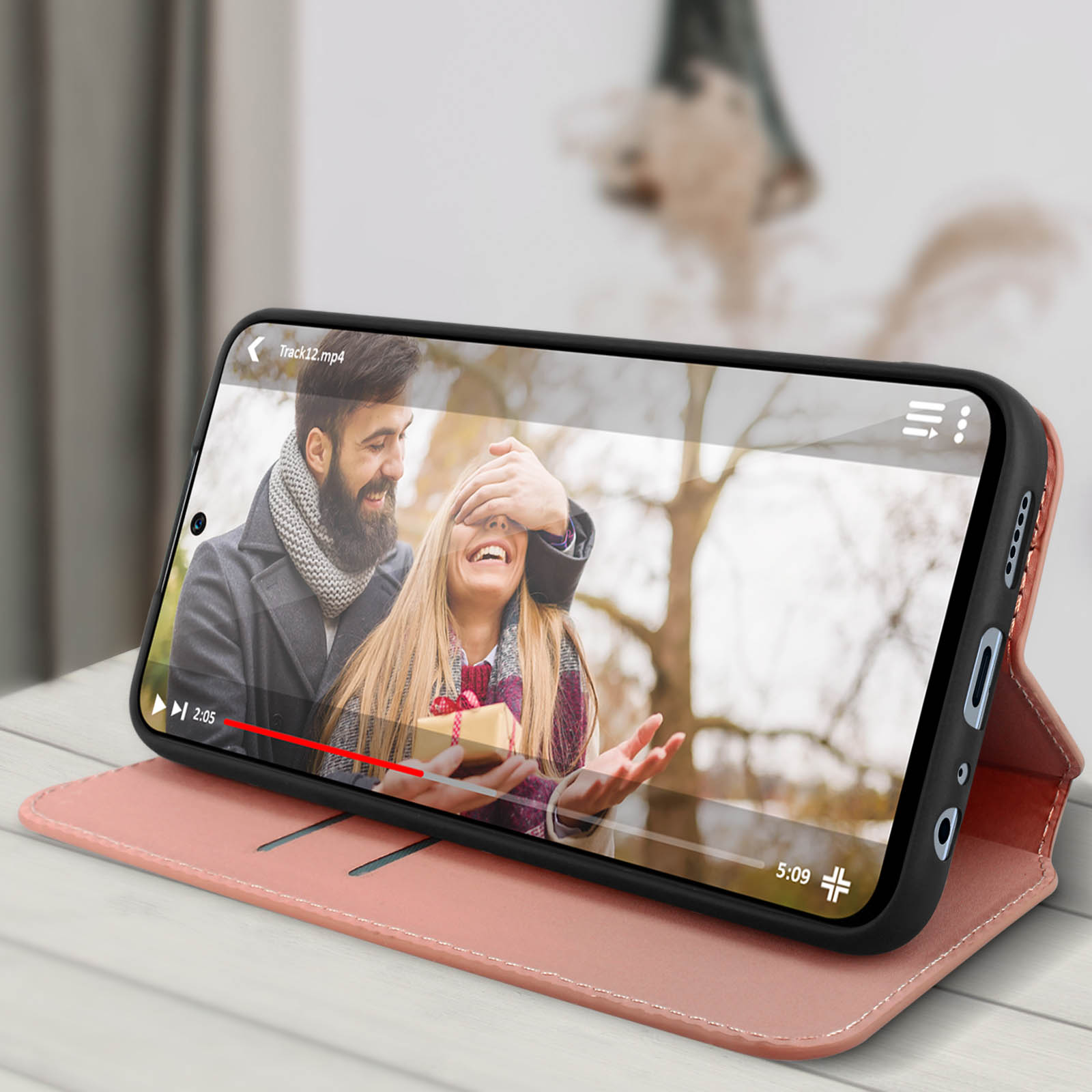 Smartphone in beigem Case mit Video eines Paares. Das Telefon liegt auf einem Tisch.