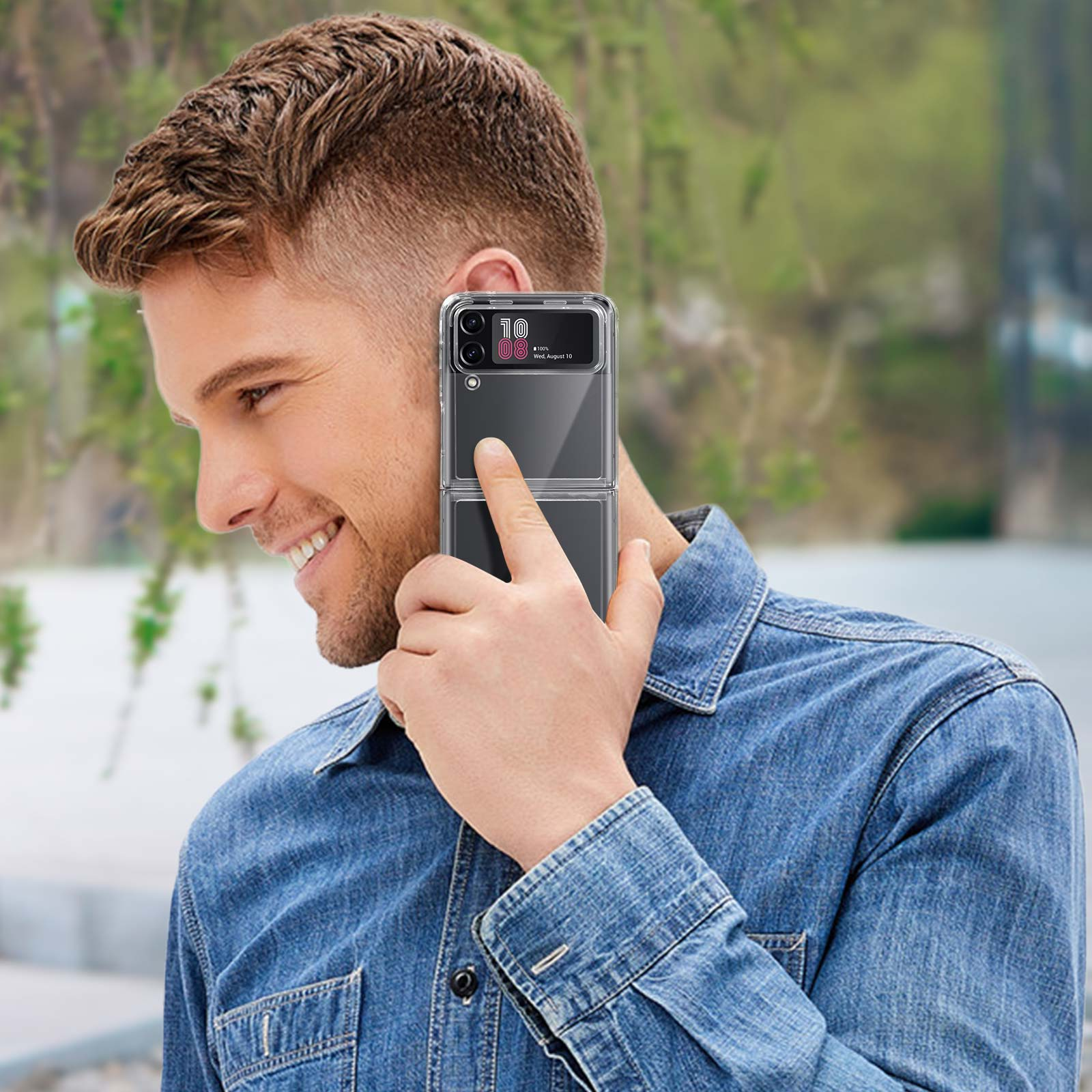 Un uomo sorridente, tiene un telefono pieghevole in una custodia trasparente. È all'aperto, con una camicia di jeans.