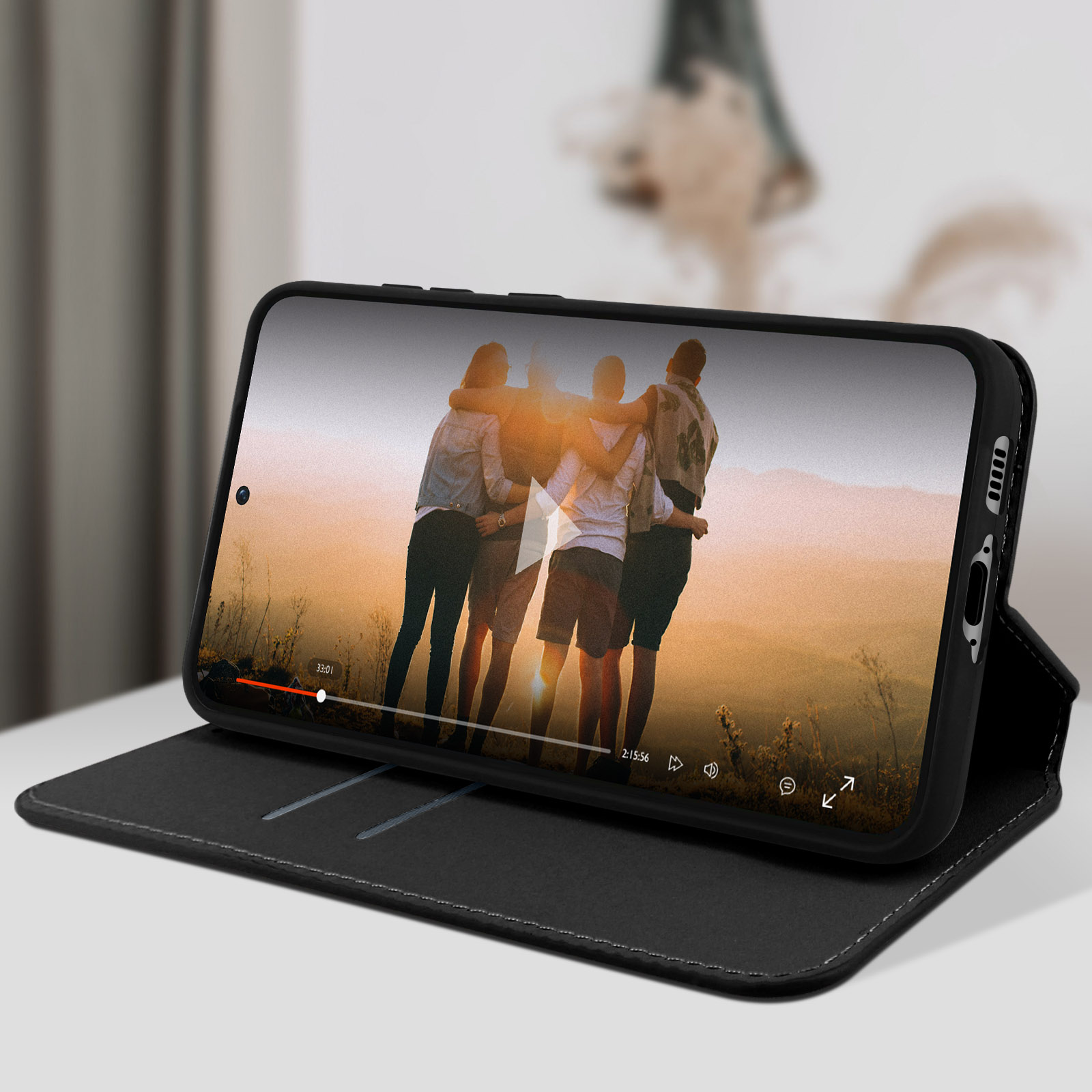 Een telefoon die een video toont van mensen die elkaar omarmen. De telefoon rust op een zwarte hoes.