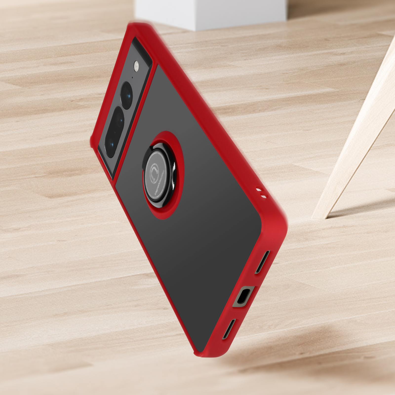 Een telefoon in een rood-zwarte hoes, met een ringhouder, rustend op een houten oppervlak.