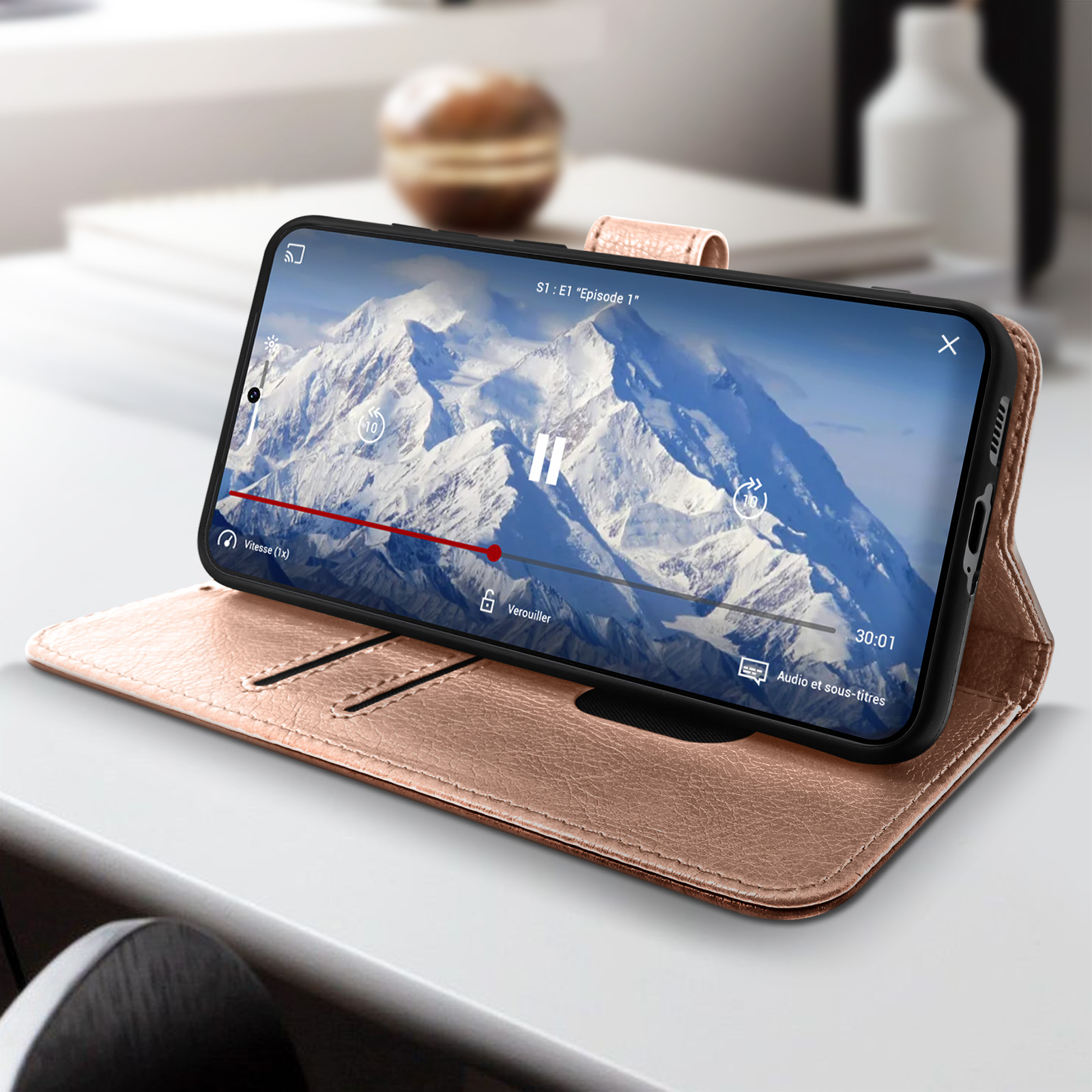 Un telefono che mostra un video su una custodia per telefono color oro rosa, con un libro sul tavolo.