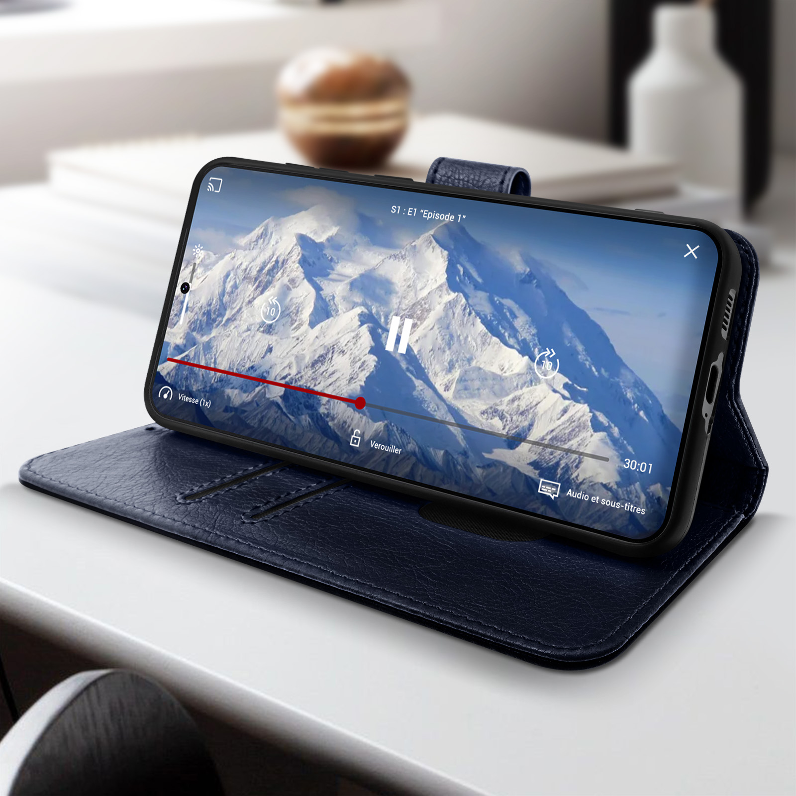 Telefoon in marineblauwe hoes toont video op wit oppervlak met boeken op de achtergrond.
