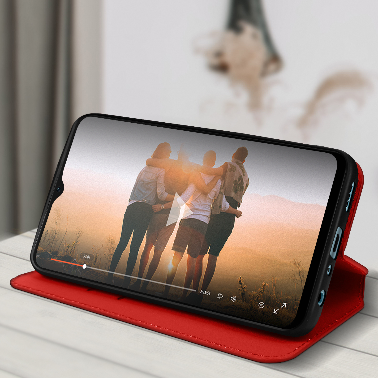 Een telefoon toont een video van mensen. De telefoon zit in een rode hoes die open ligt op een tafel.