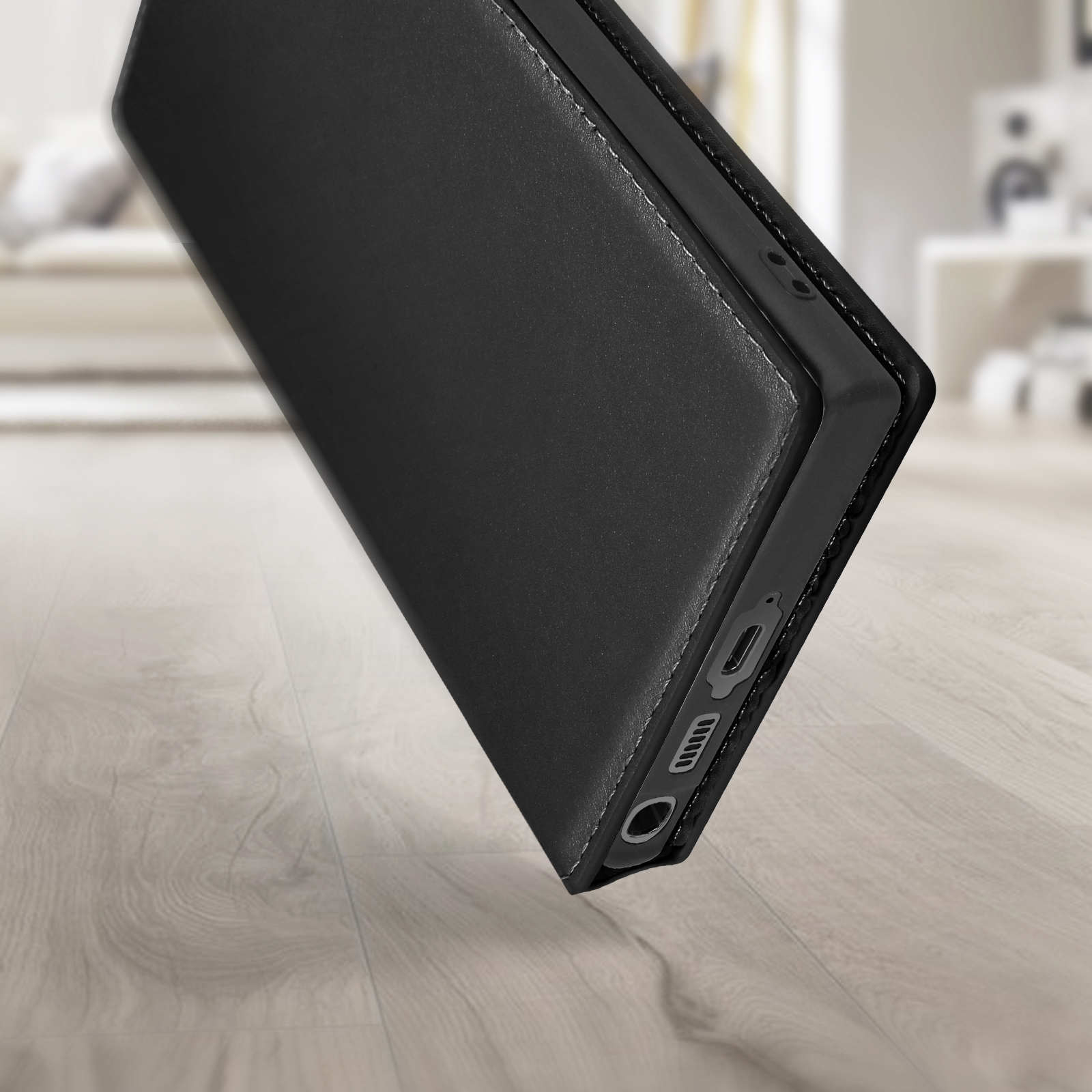 Een zwarte telefoonhoes staat schuin op een houten oppervlak. De achtergrond is wazig.