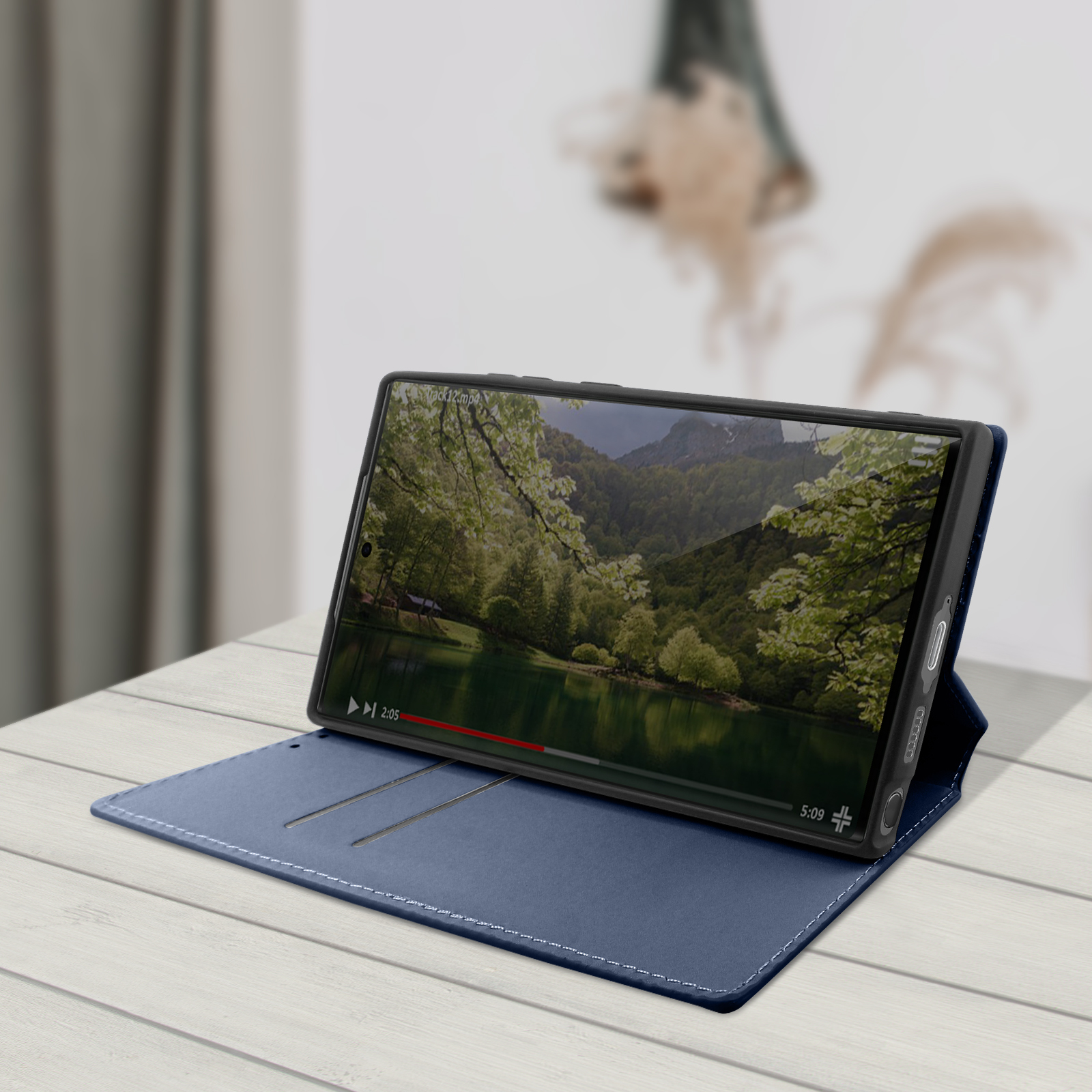 Telefoon in een blauwe hoes, omhooggeklapt, toont een video. De omgeving is binnenshuis.