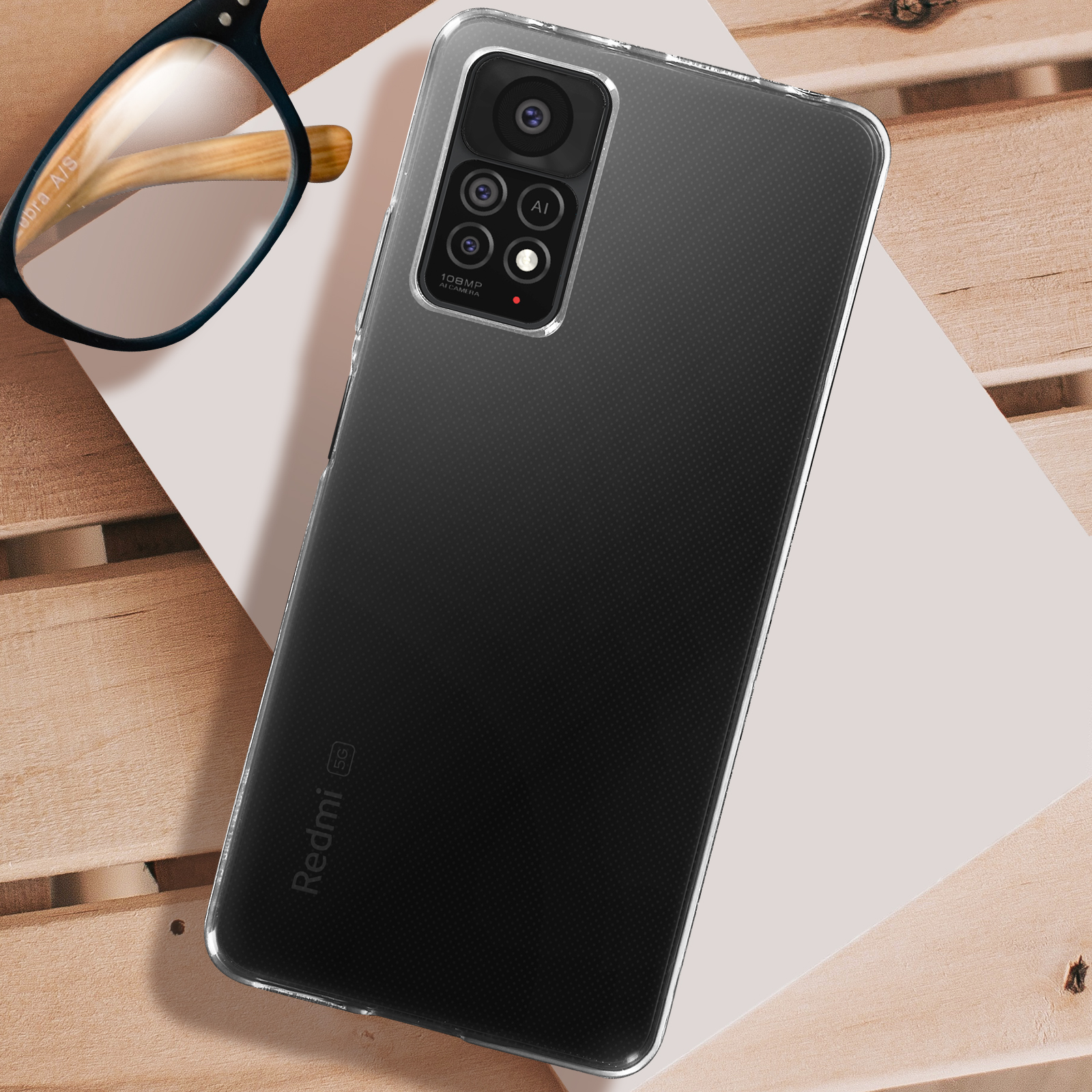 Handyhülle auf Holzoberfläche. Transparente Hülle mit Kameradetails. Redmi-Logo sichtbar.