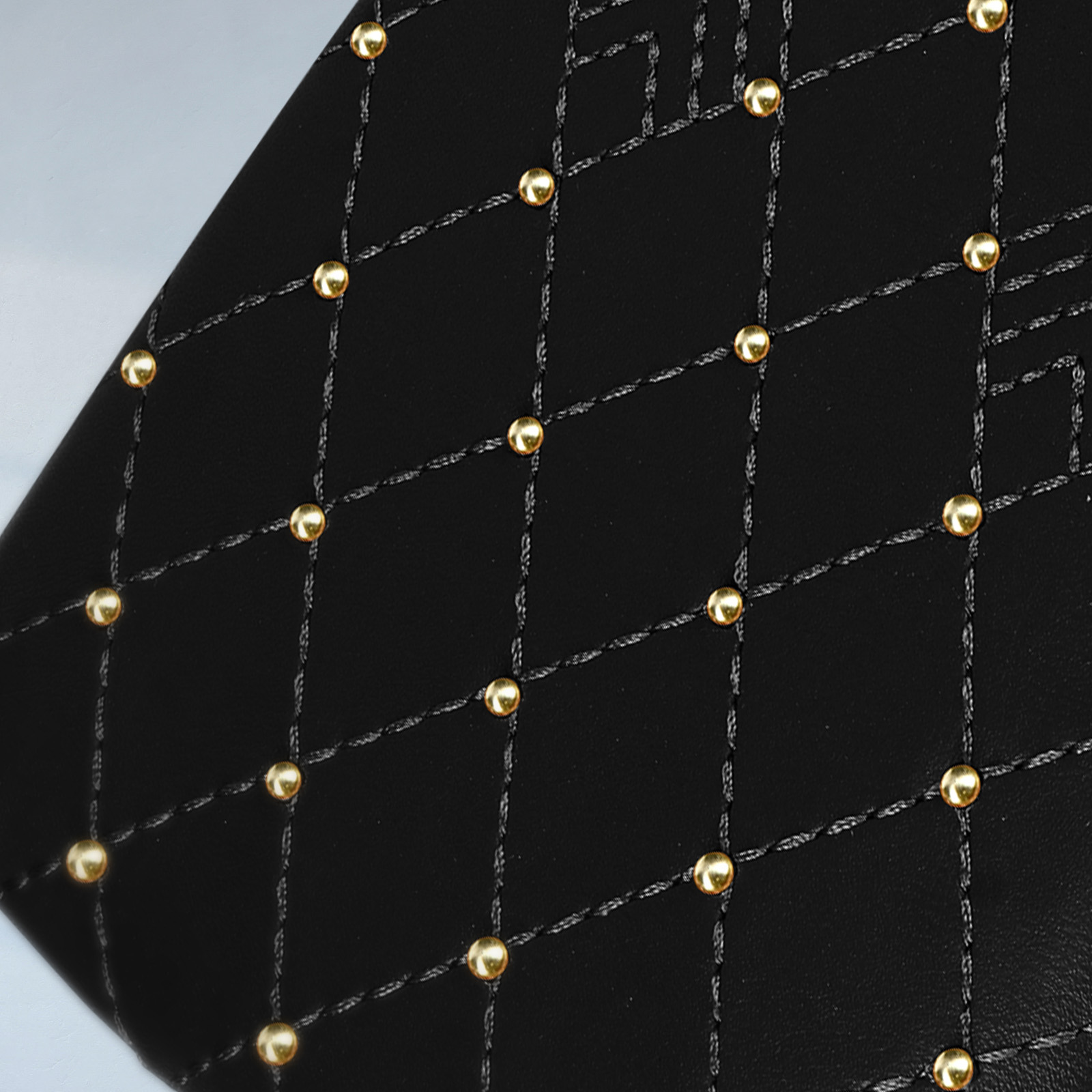 Un primo piano di materiale nero con un motivo a rombi e borchie dorate spaziate uniformemente.